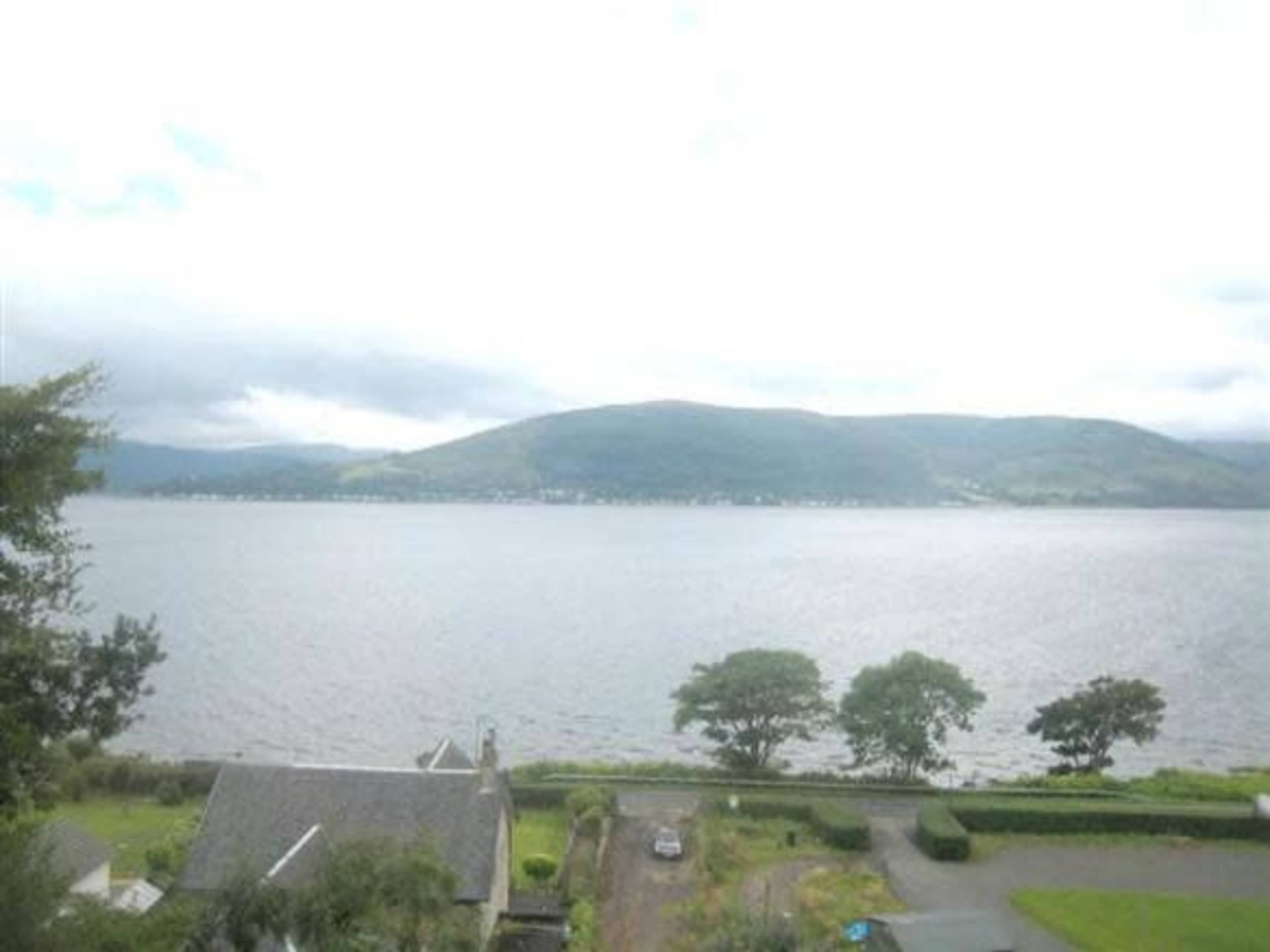 A calm lake surrounded by hills, with a house and a pathway in the foreground.