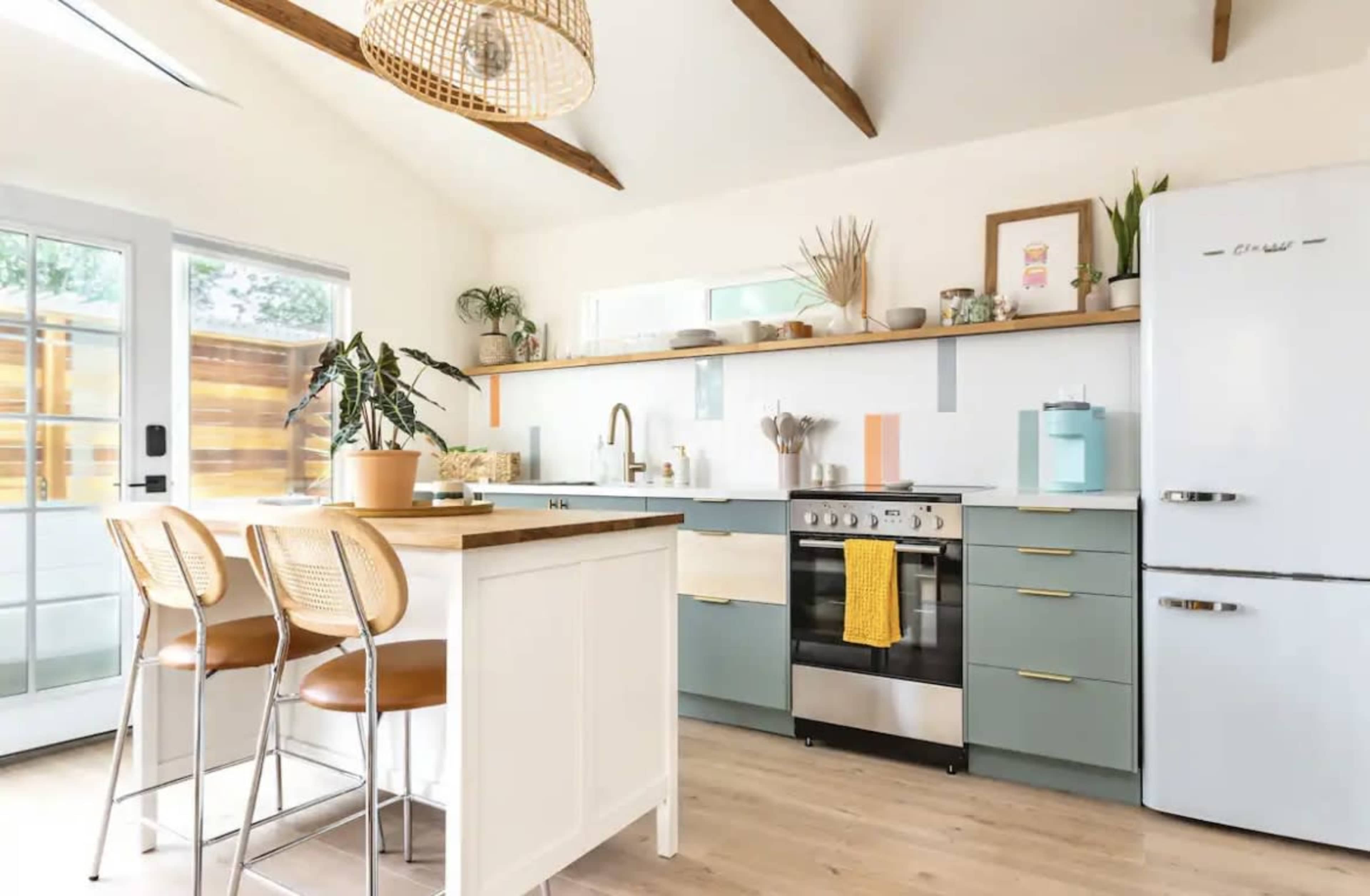 A modern kitchen features a central island with bar stools, a stove, and open shelving adorned with plants and decorative items.