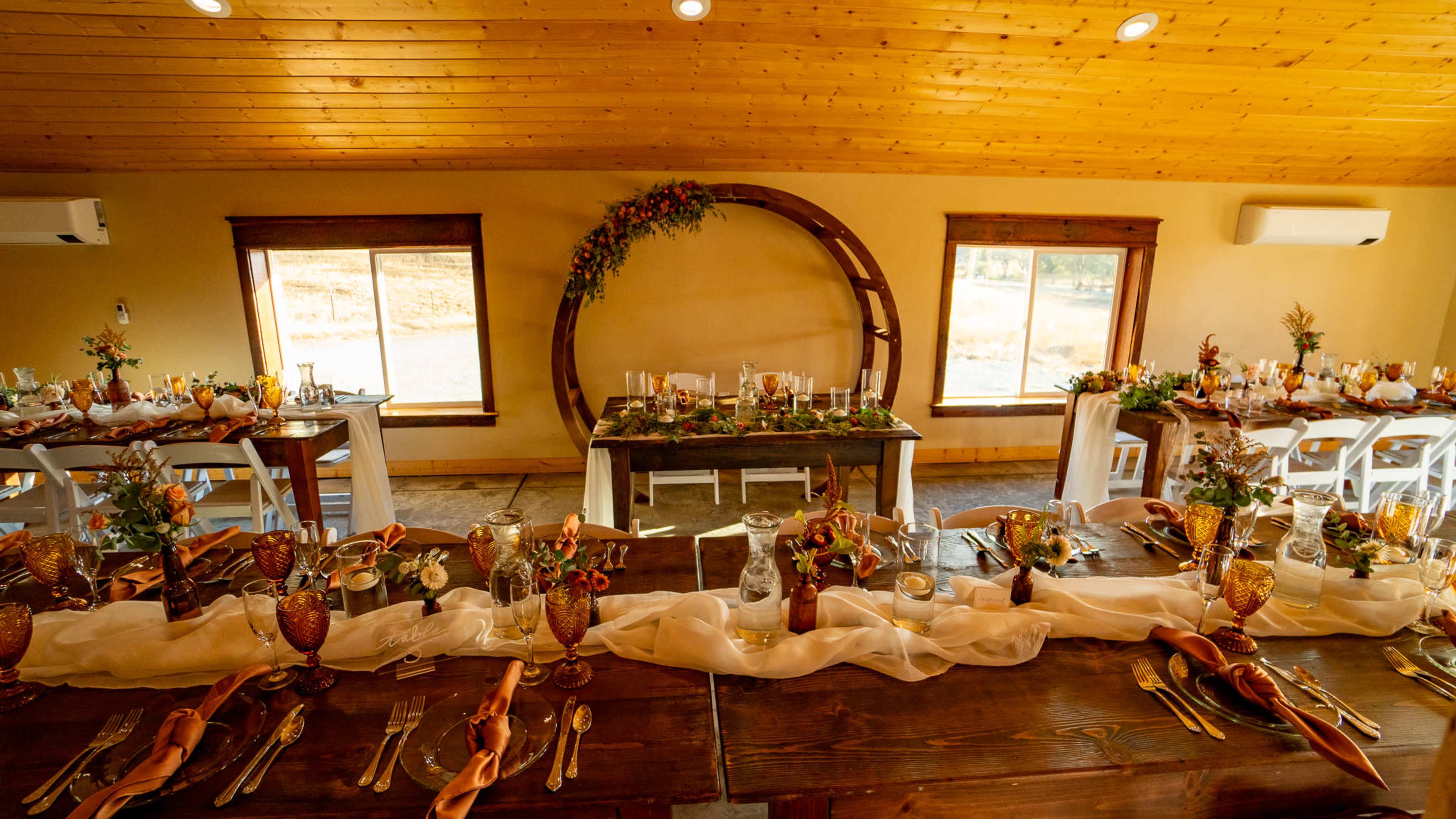 A decorated dining area features wooden tables set with elegant tableware and floral arrangements under warm lighting.