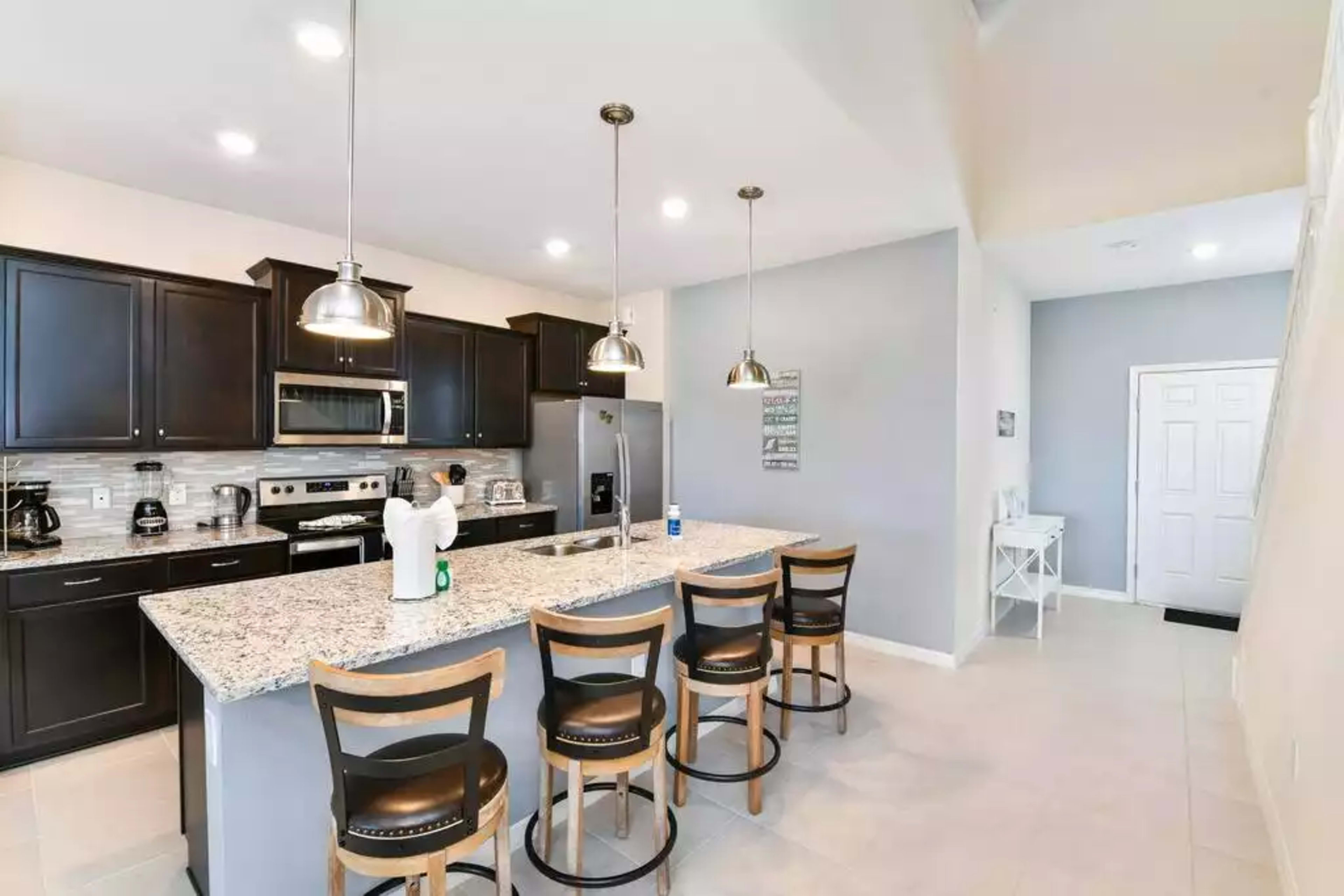A modern kitchen with a large island, black cabinetry, stainless steel appliances, and barstool seating.