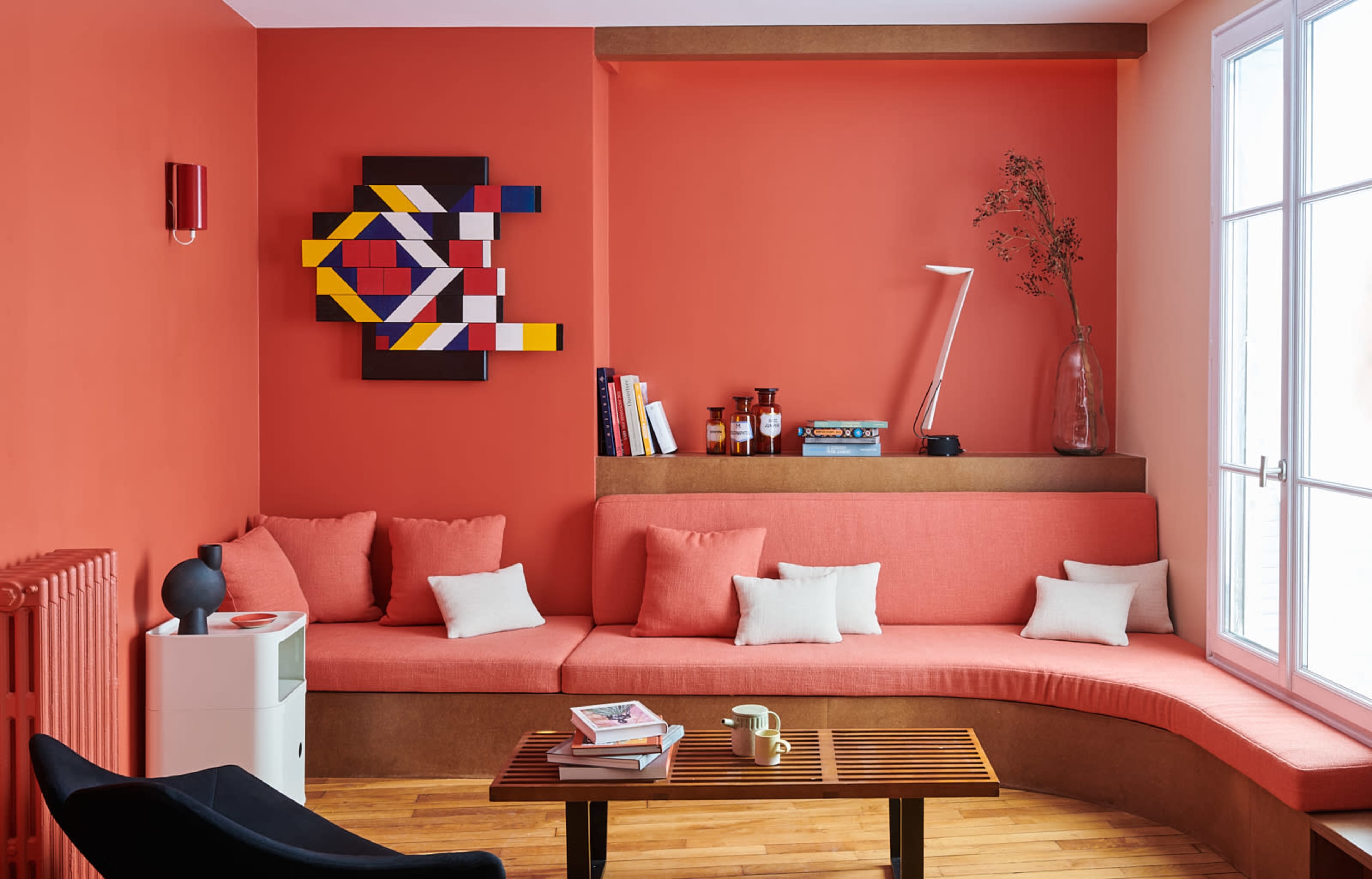 A cozy corner of a room featuring a curved bench with orange cushions, a wooden coffee table, and a colorful abstract artwork on the wall.