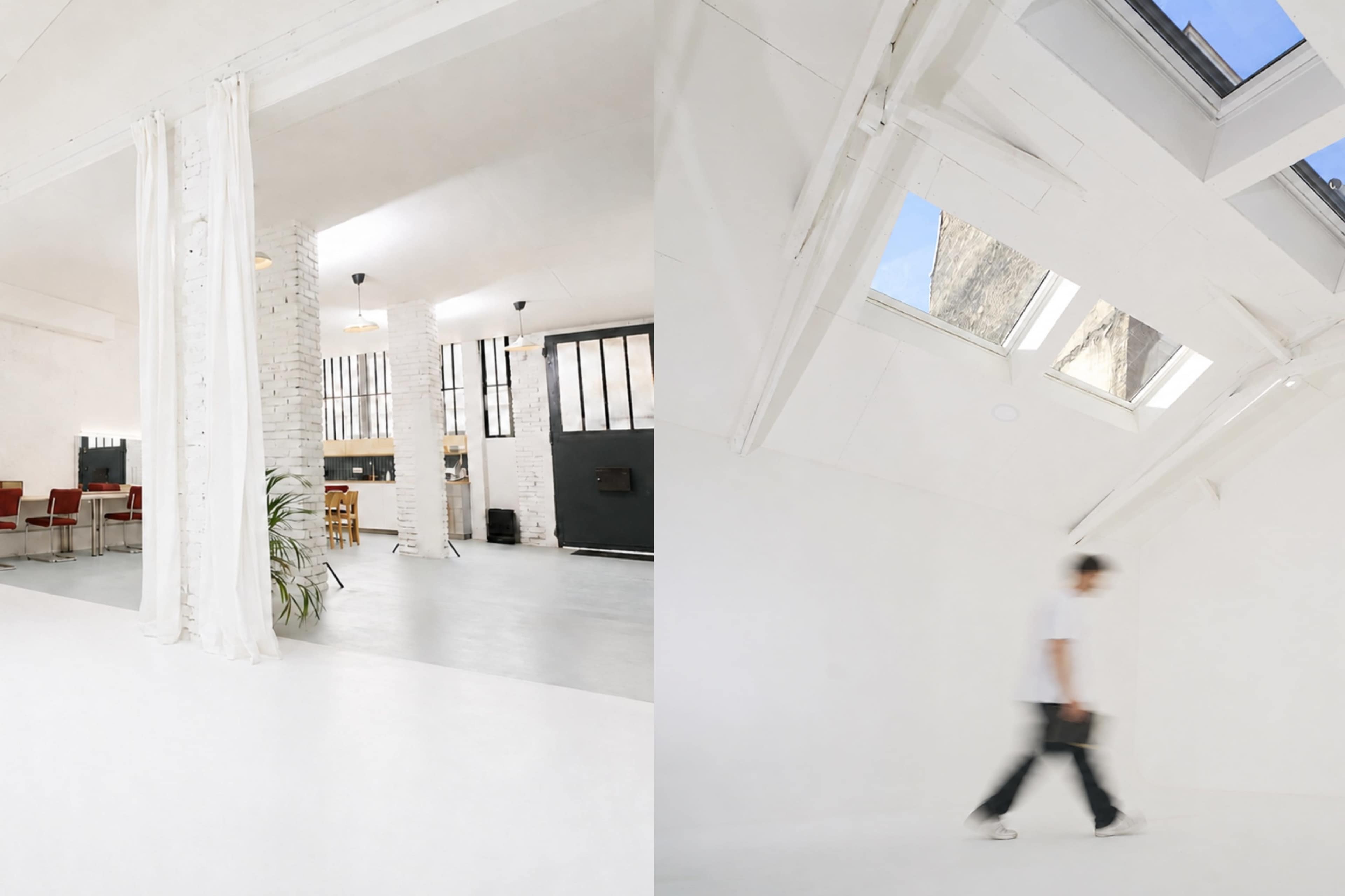 The image shows a bright, airy room featuring white walls and high ceilings, with a person walking through the space.