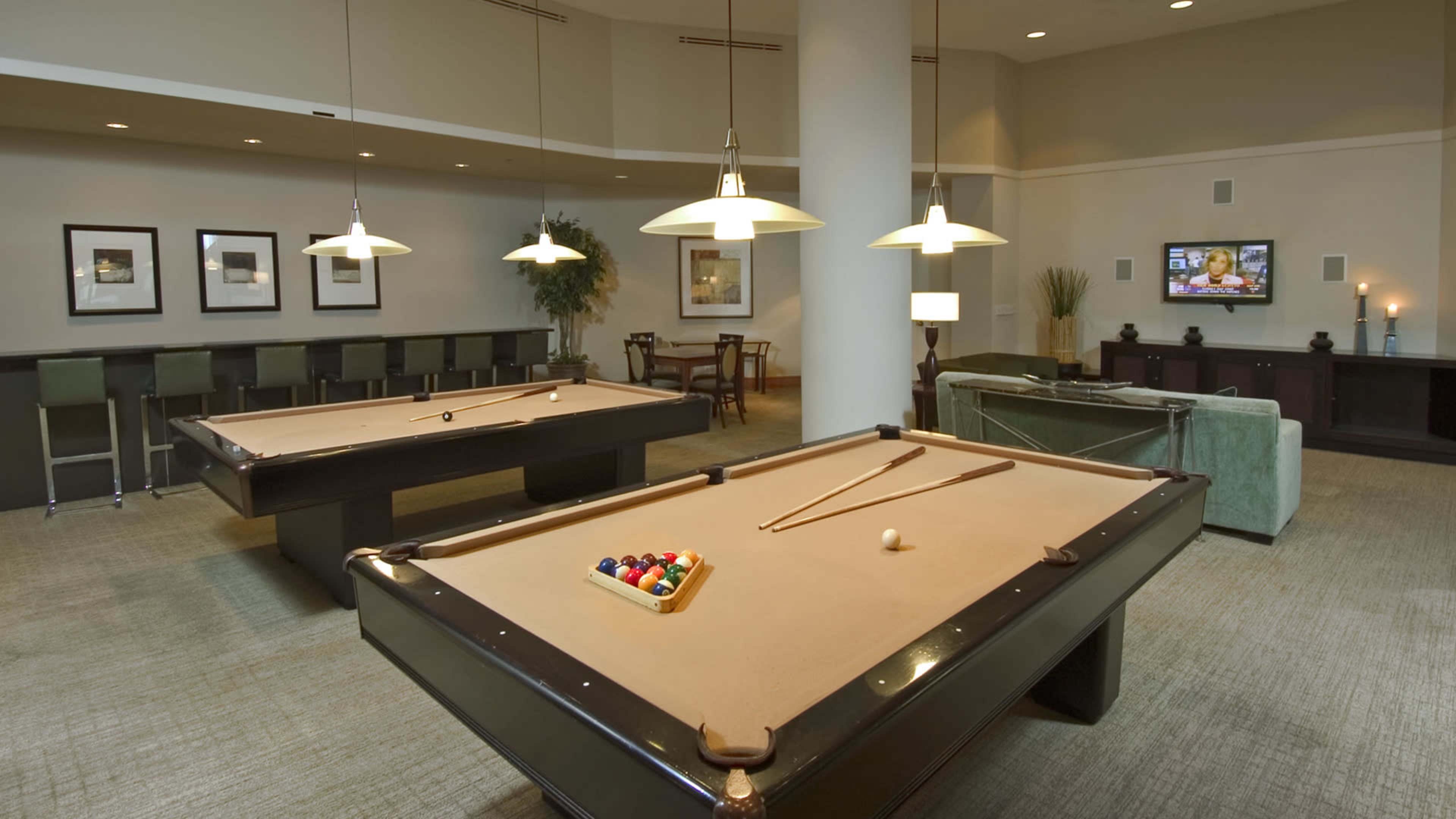 A game room with two billiard tables, seating areas, and framed artwork on the walls.