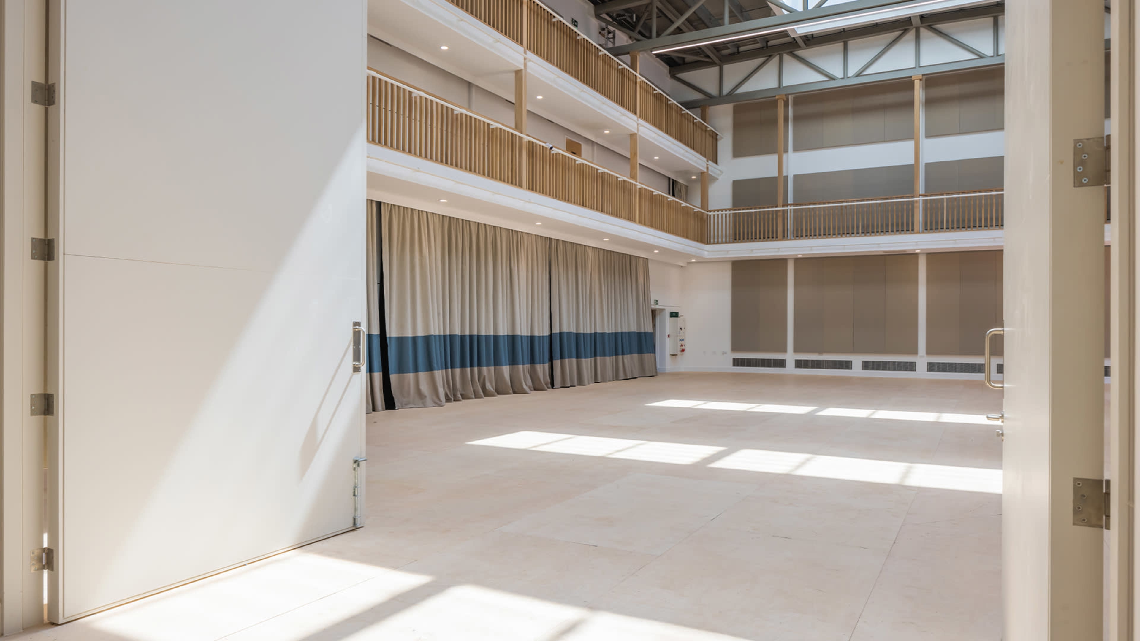 A large, empty indoor space with tall ceilings, natural light streaming in through doors, and curtains along the walls.