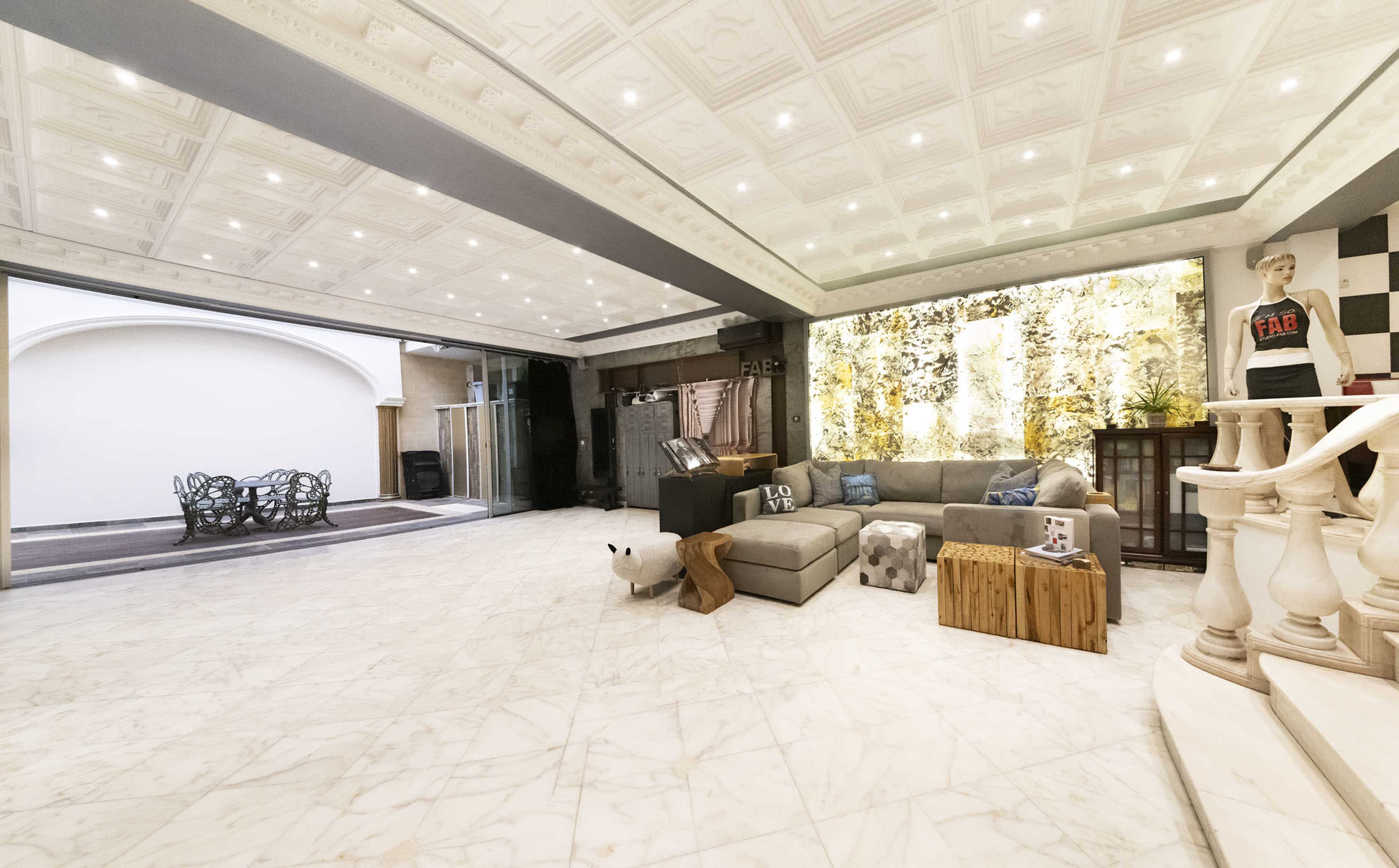 A spacious, modern interior with a marble floor, a large sectional sofa, and decorative wall features illuminated by ceiling lights.