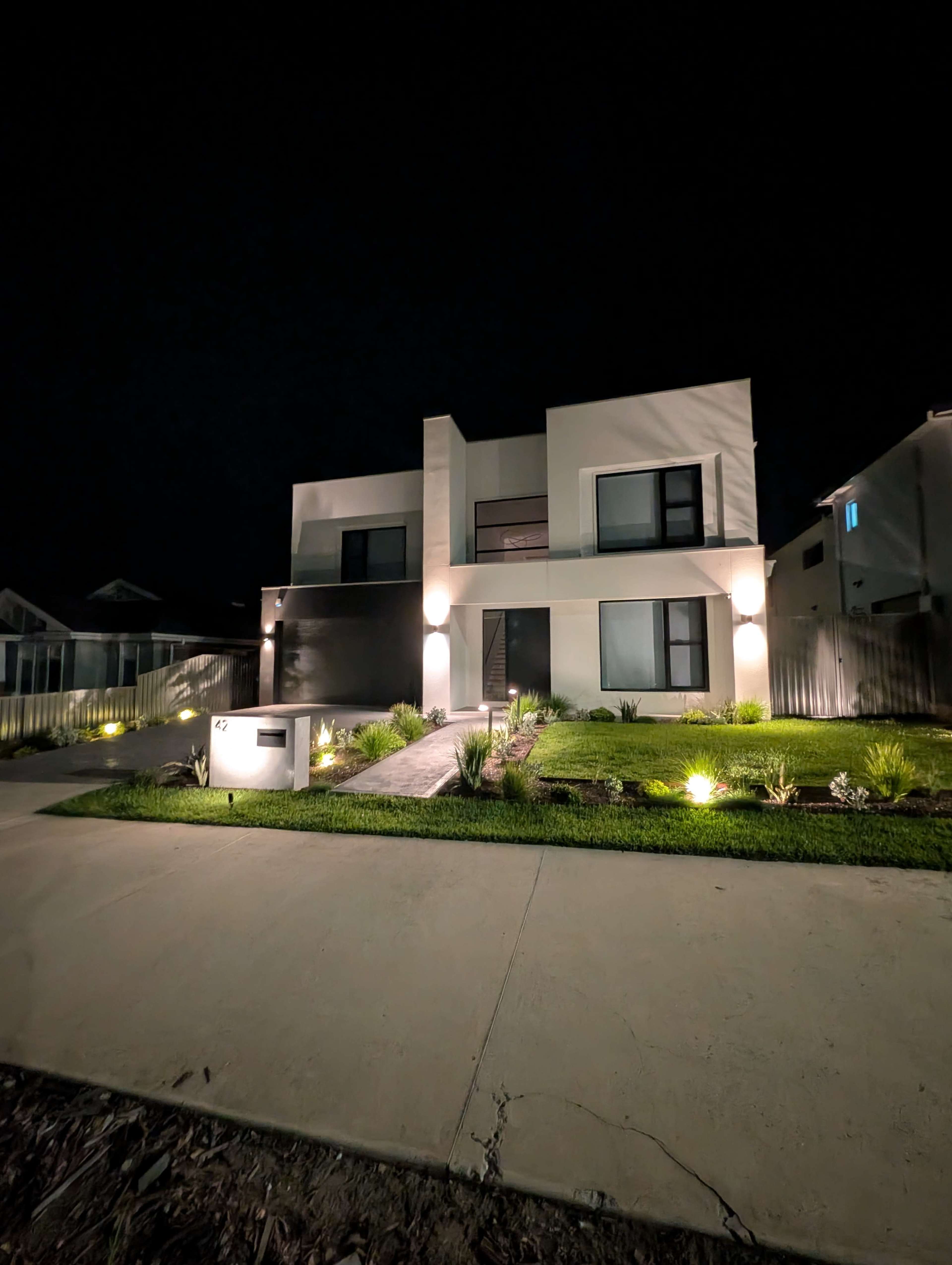 A modern two-story house with exterior lighting and a neatly landscaped front yard is prominently featured at night.