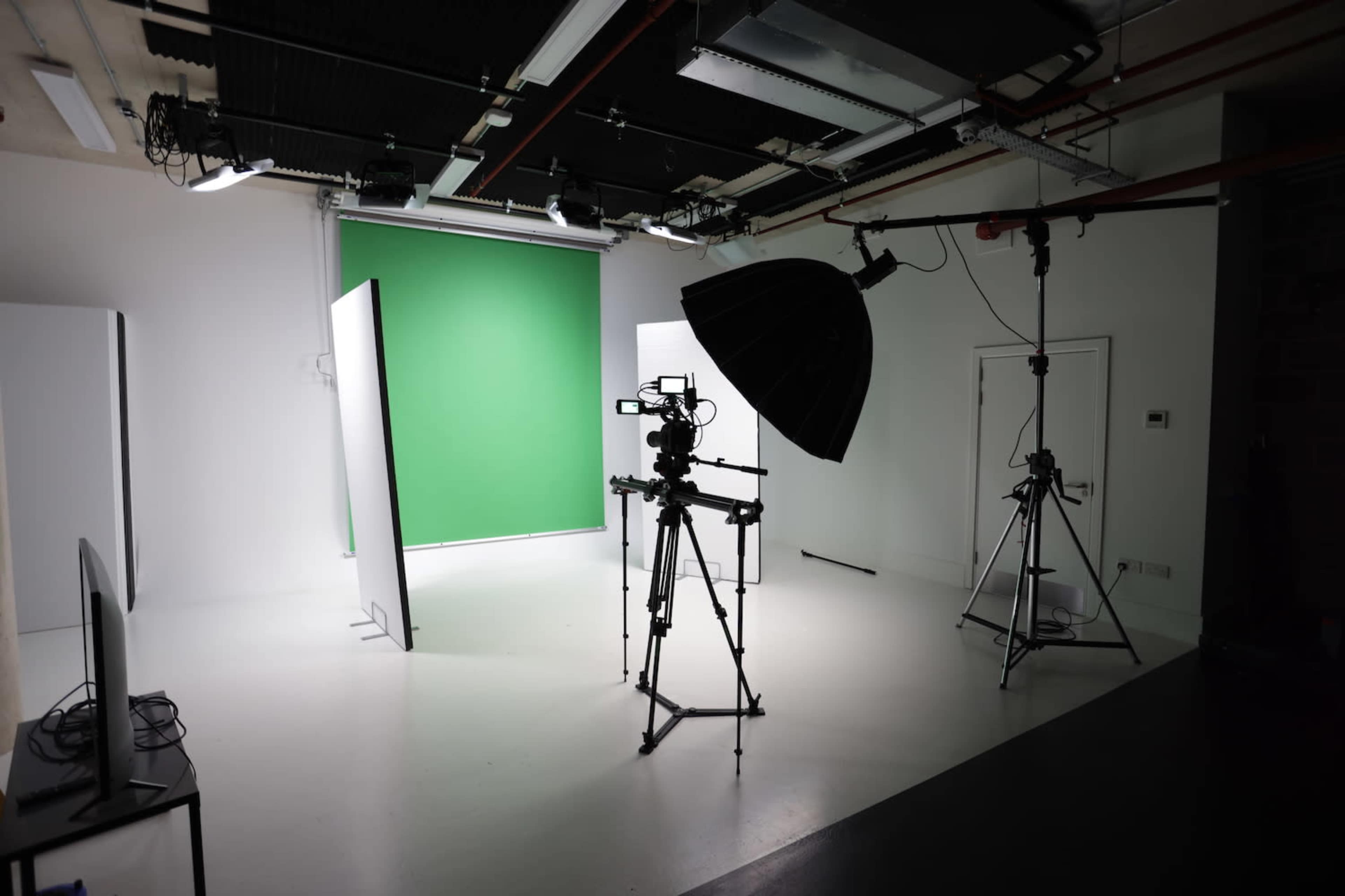 A photography studio is set up with a green screen, lighting equipment, and cameras on tripods.