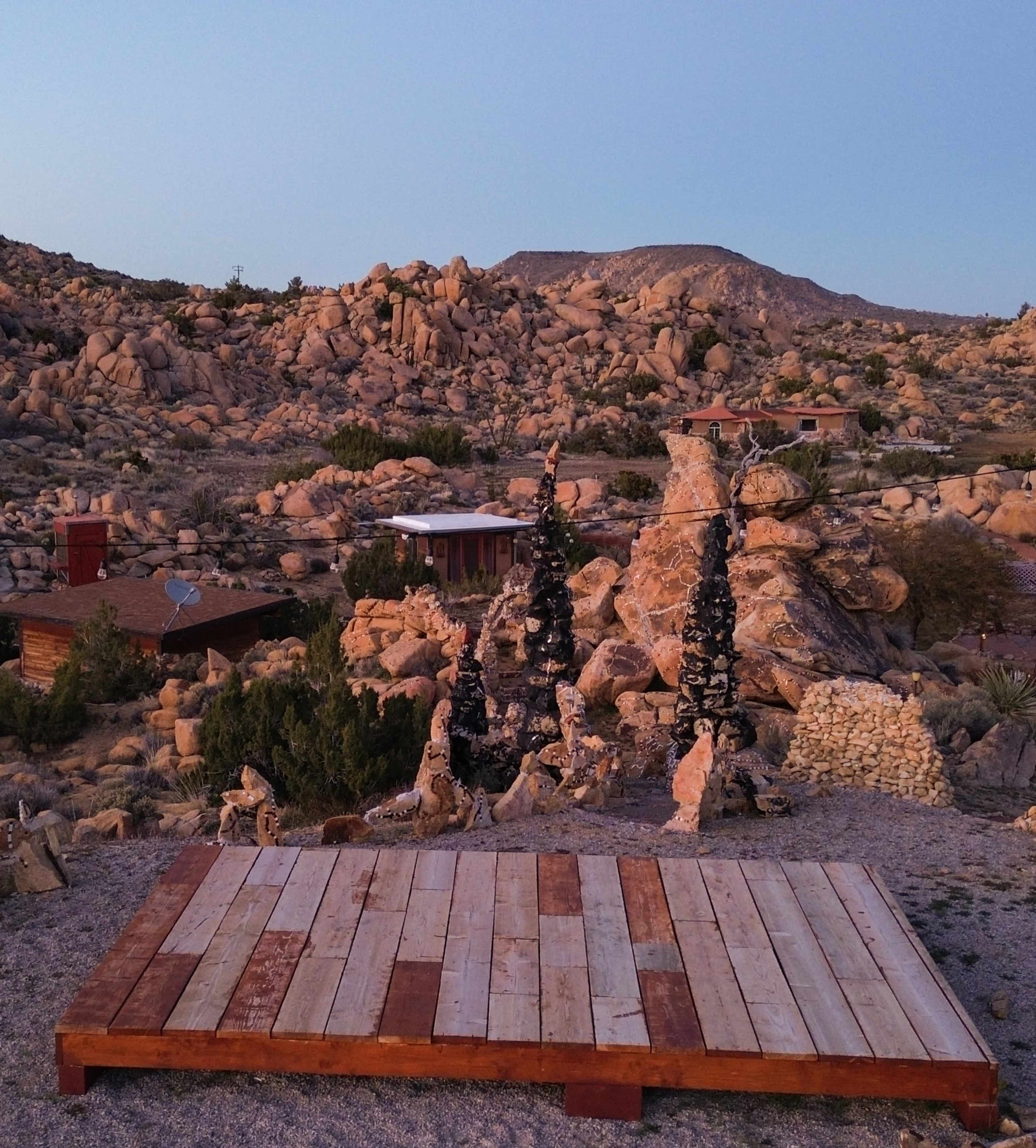 The image shows a wooden platform surrounded by rocky terrain and sparse vegetation in a desert landscape.