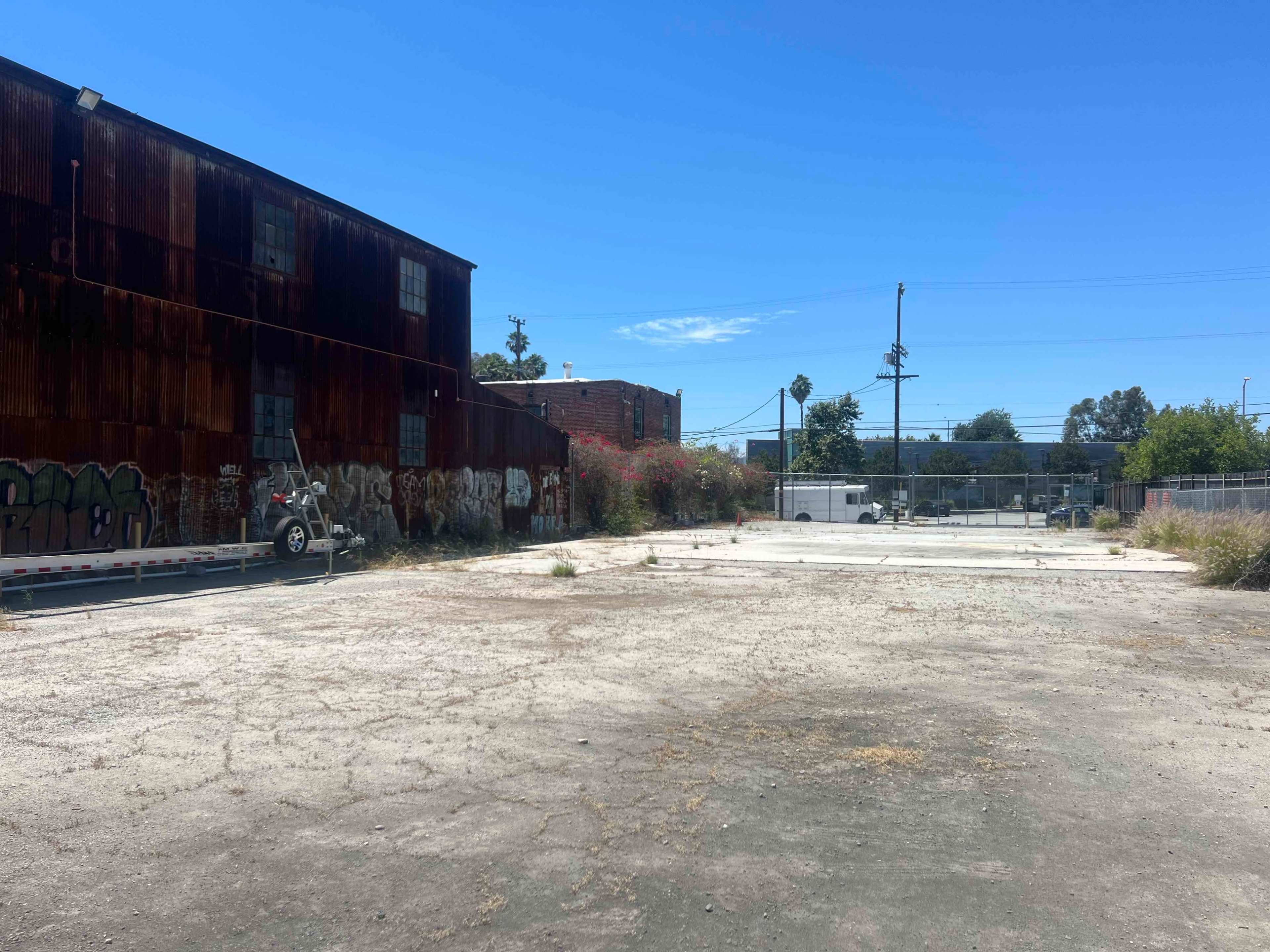 An empty, cracked lot surrounded by rusted buildings and graffiti-covered walls under a clear blue sky.