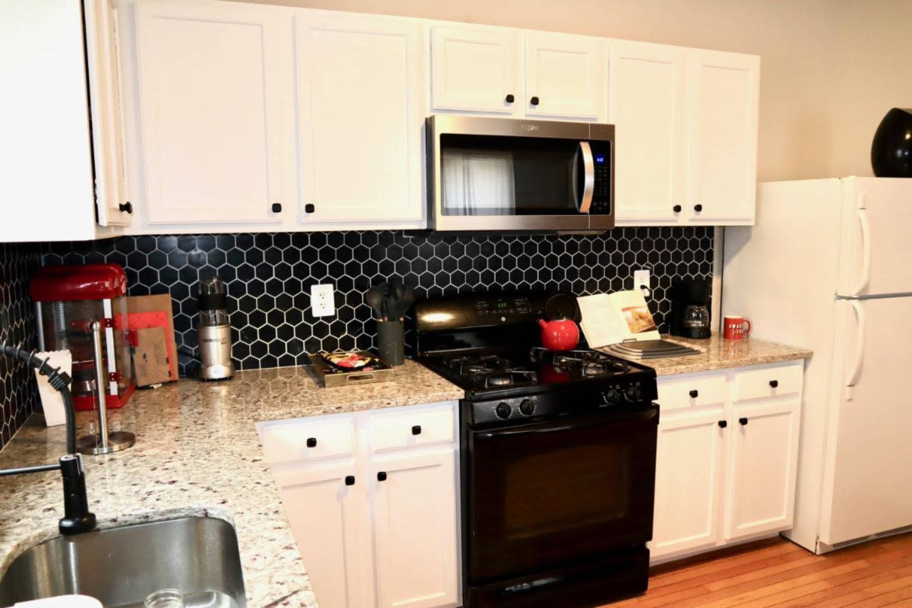 A kitchen with white cabinets, a black stove, a microwave, and a countertop made of speckled granite, along with a hexagonal tiled backsplash.