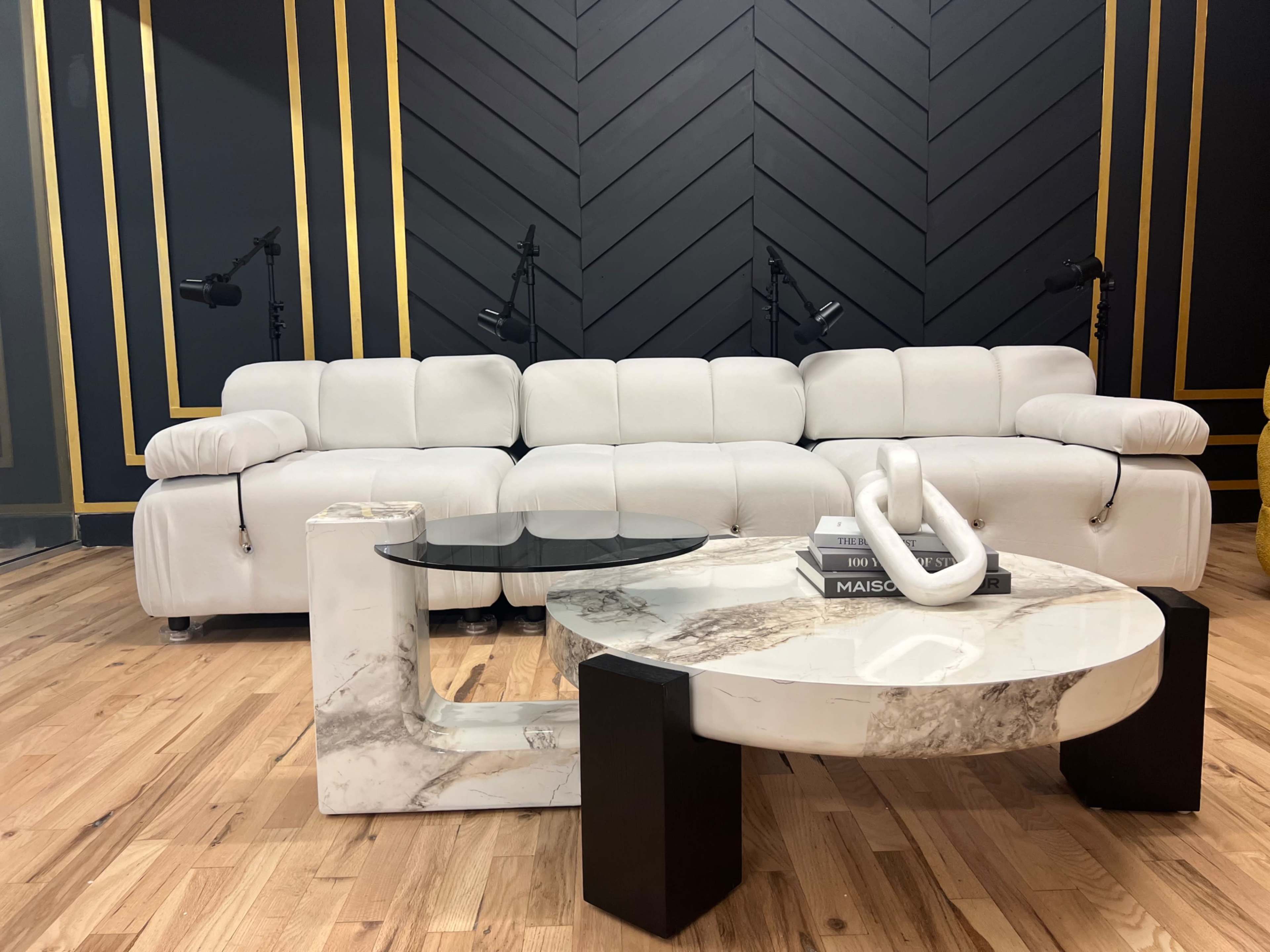 A modern living room setup featuring a white sectional sofa and two distinct coffee tables, one circular and one rectangular, both with marble and black accents.