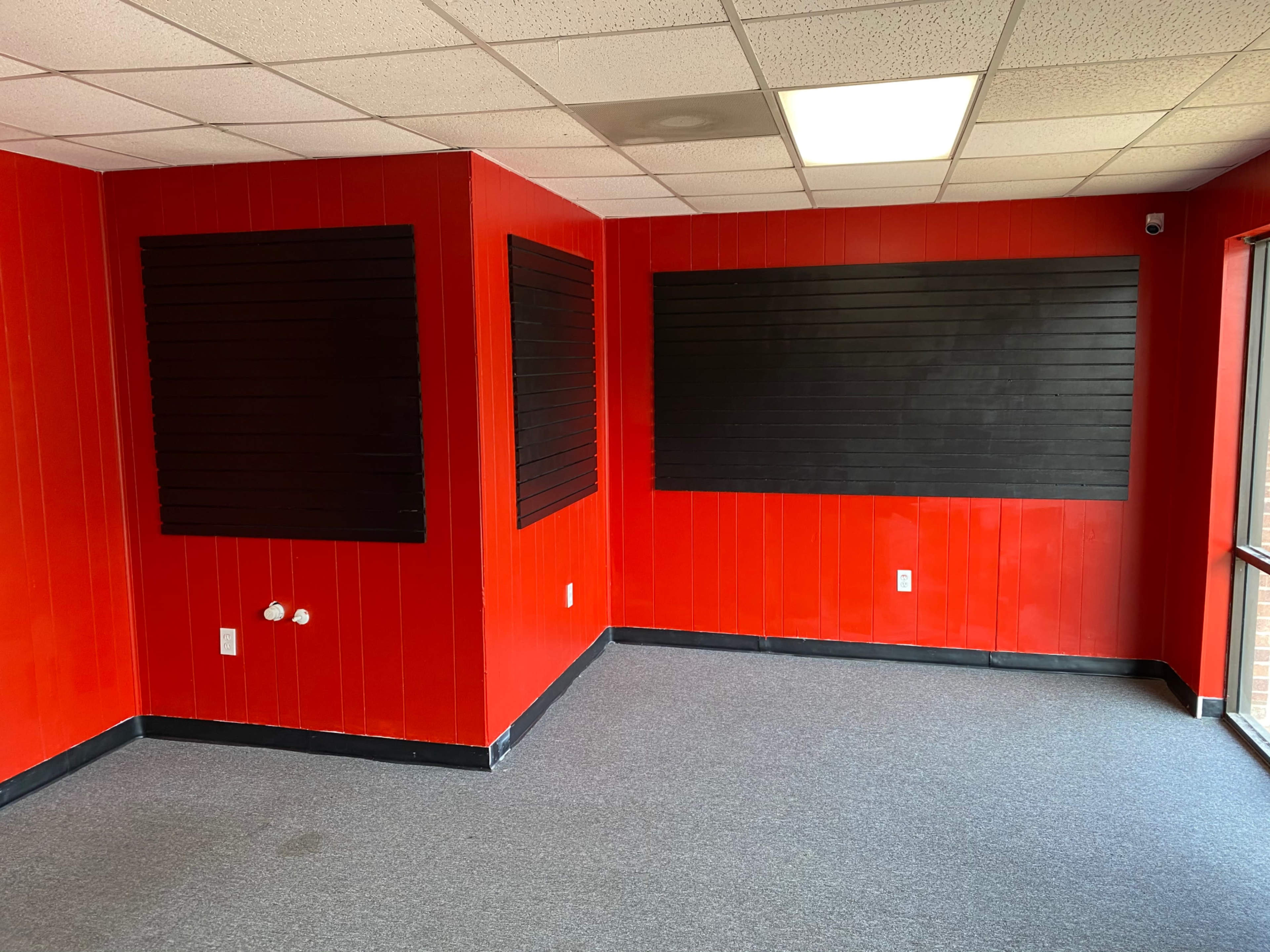 A room with red walls, black wooden wall panels, and gray carpeting.