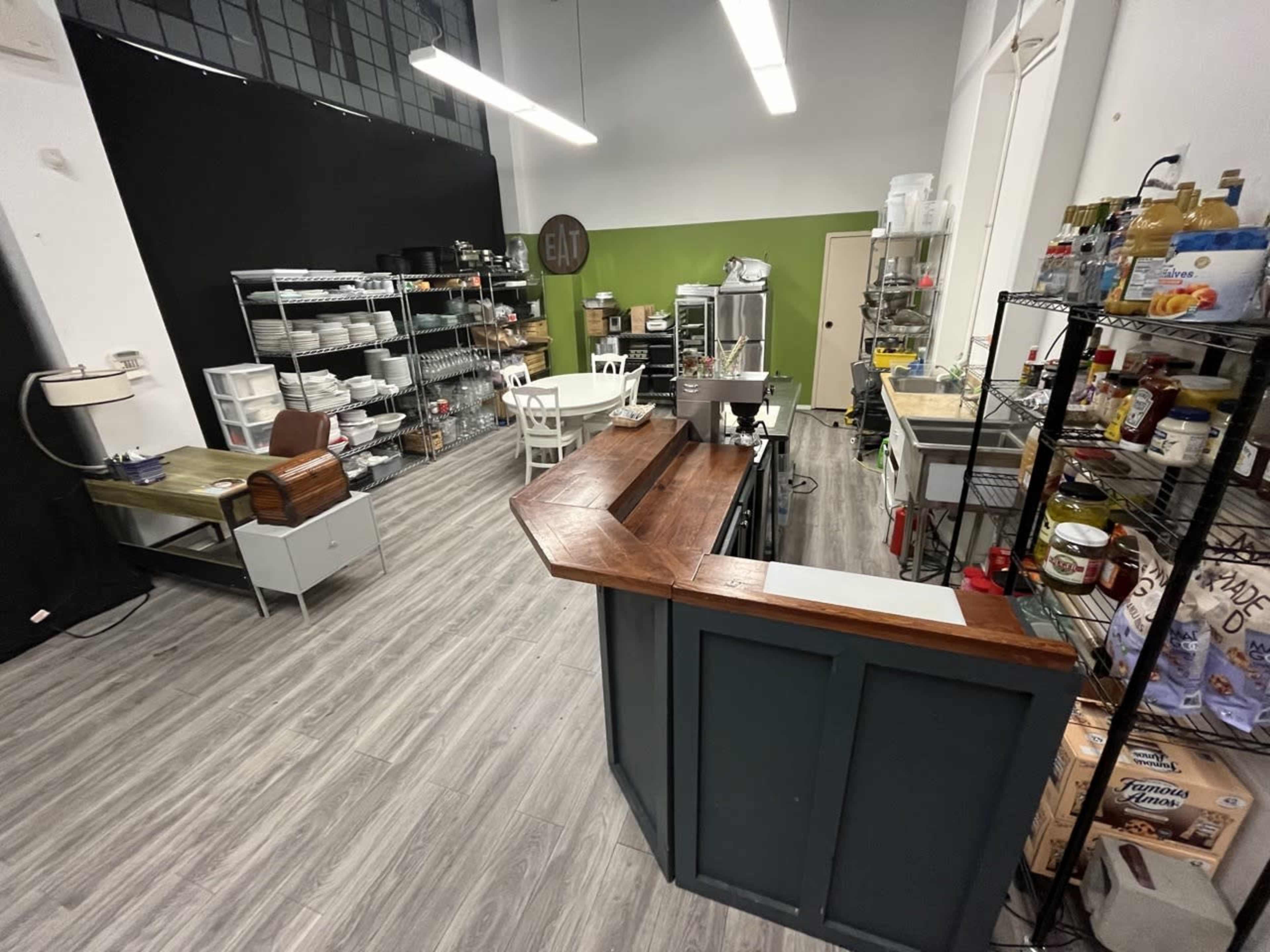 A modern kitchen space with a wooden counter, shelves filled with ingredients, and various kitchen equipment arranged neatly.