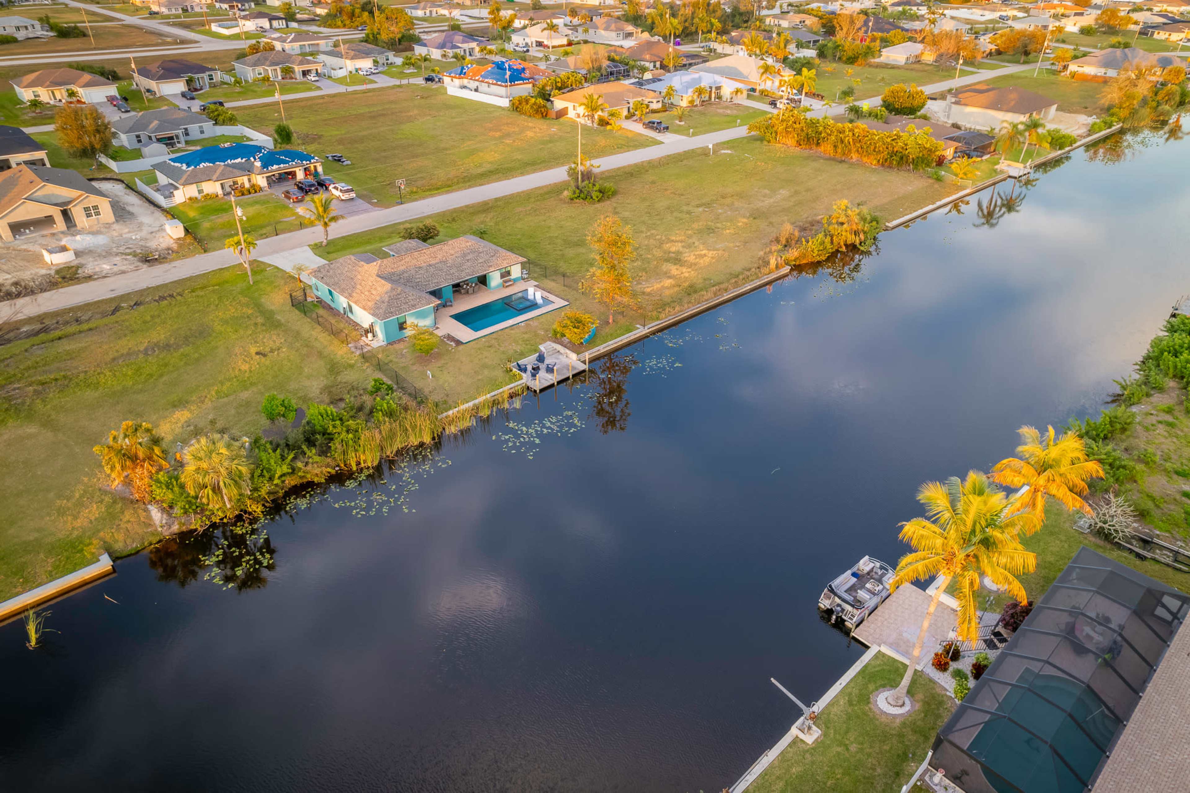 A residential neighborhood with houses lining a canal, featuring a backyard pool and greenery along the water's edge.