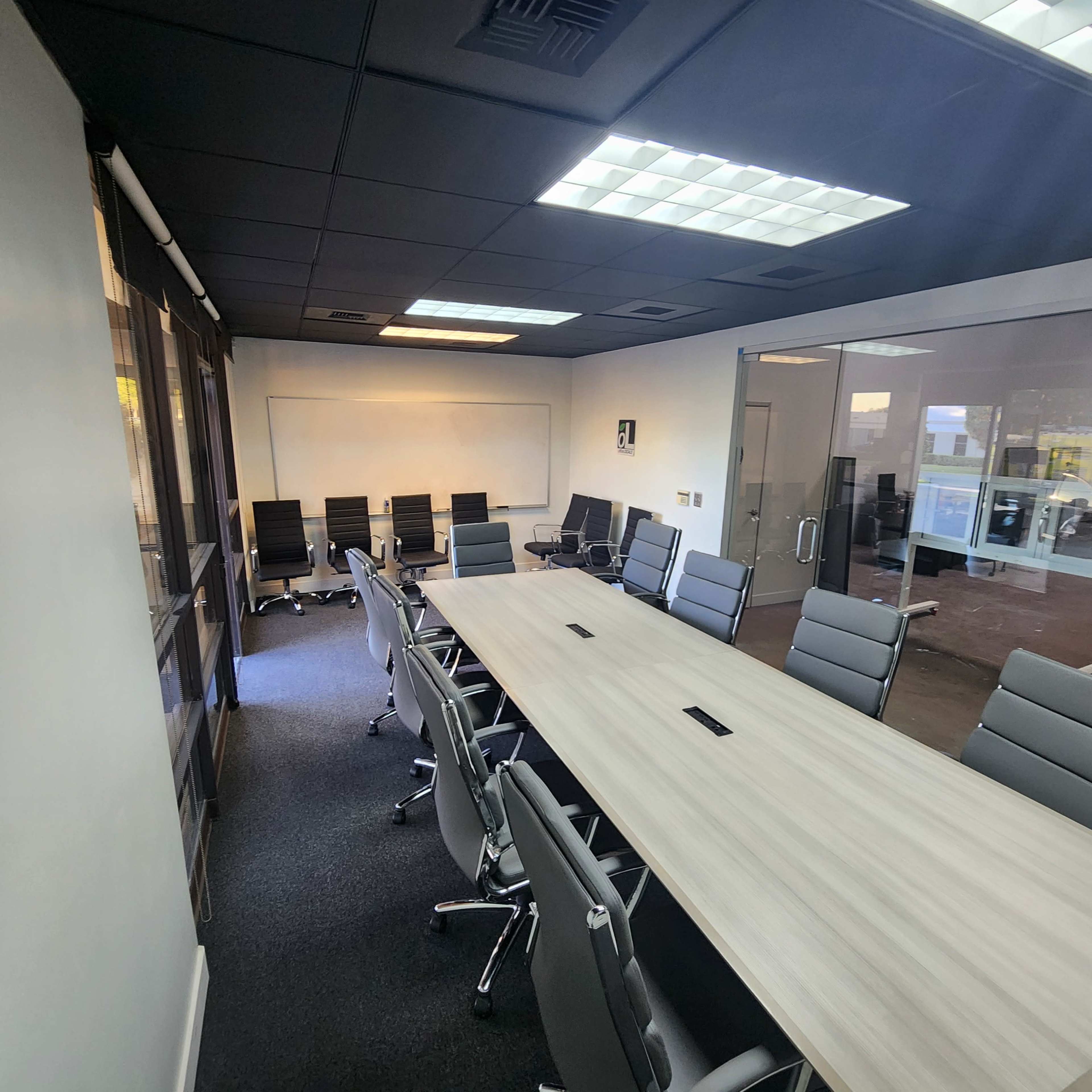 A large conference room features a long table surrounded by modern chairs, with a whiteboard and glass walls.