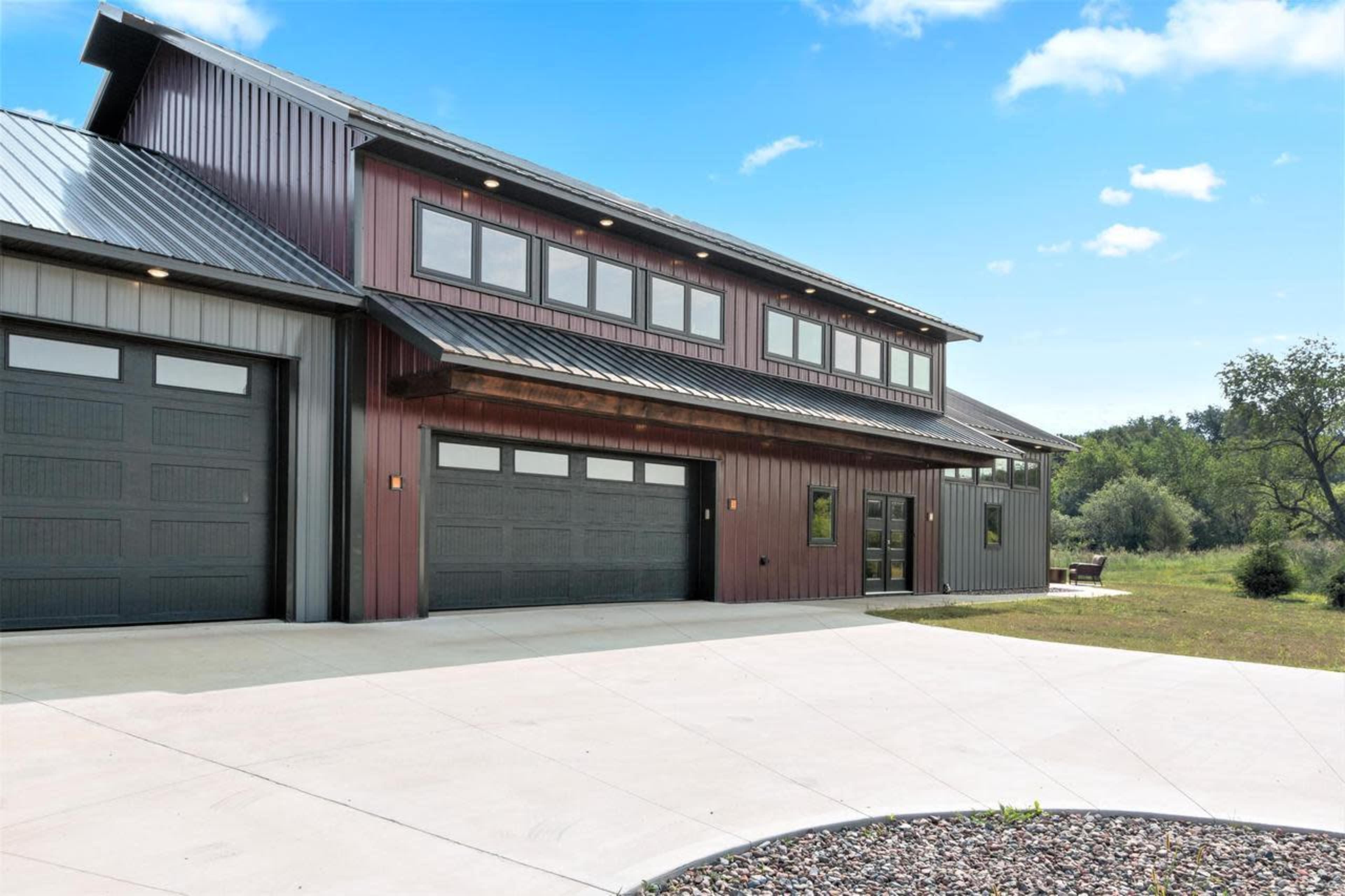 A modern, two-story building with a metal exterior features large windows and multiple garage doors, set against a clear blue sky and green landscape.