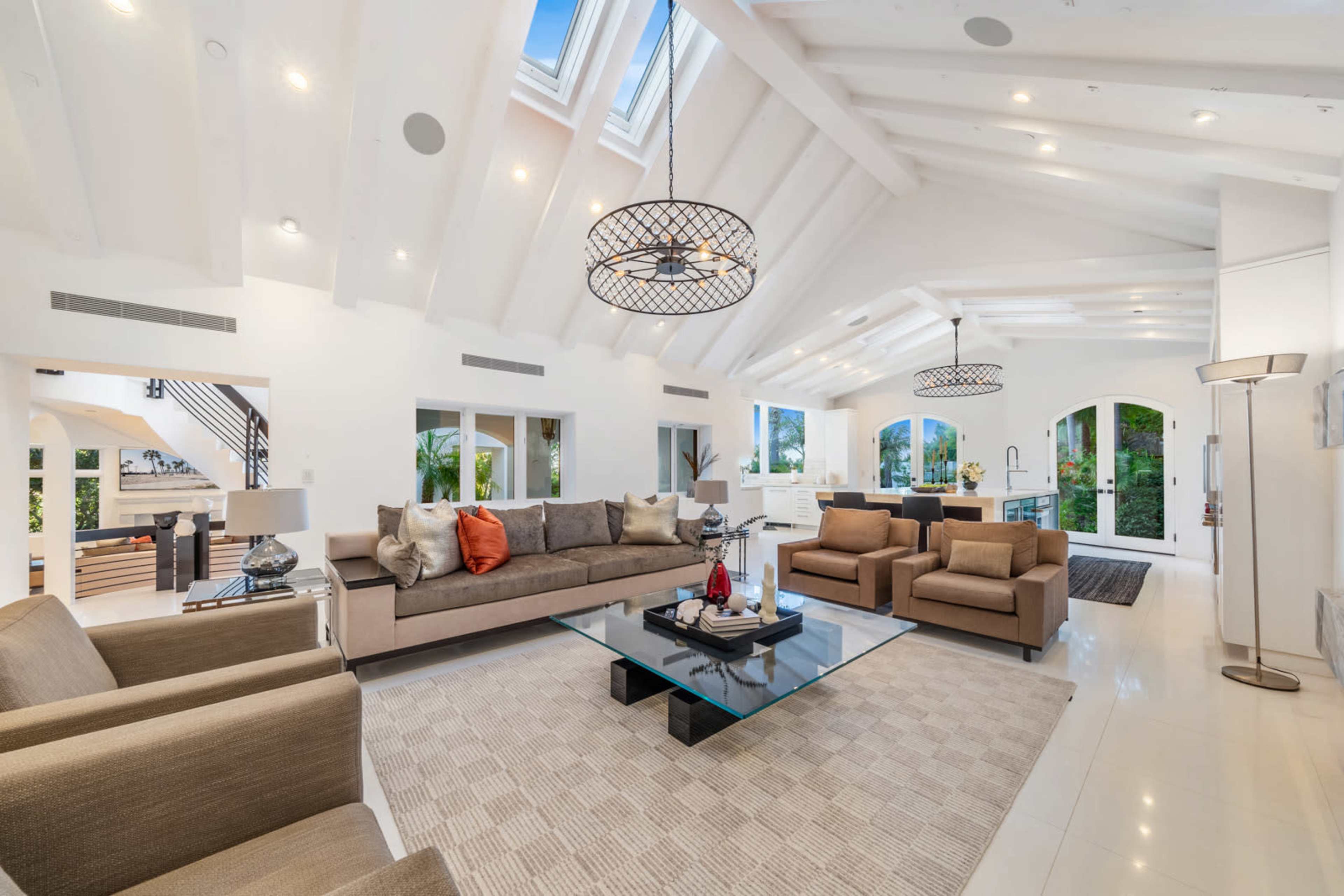 A spacious, modern living room with high ceilings, large windows, and stylish furniture, featuring a glass coffee table at the center.