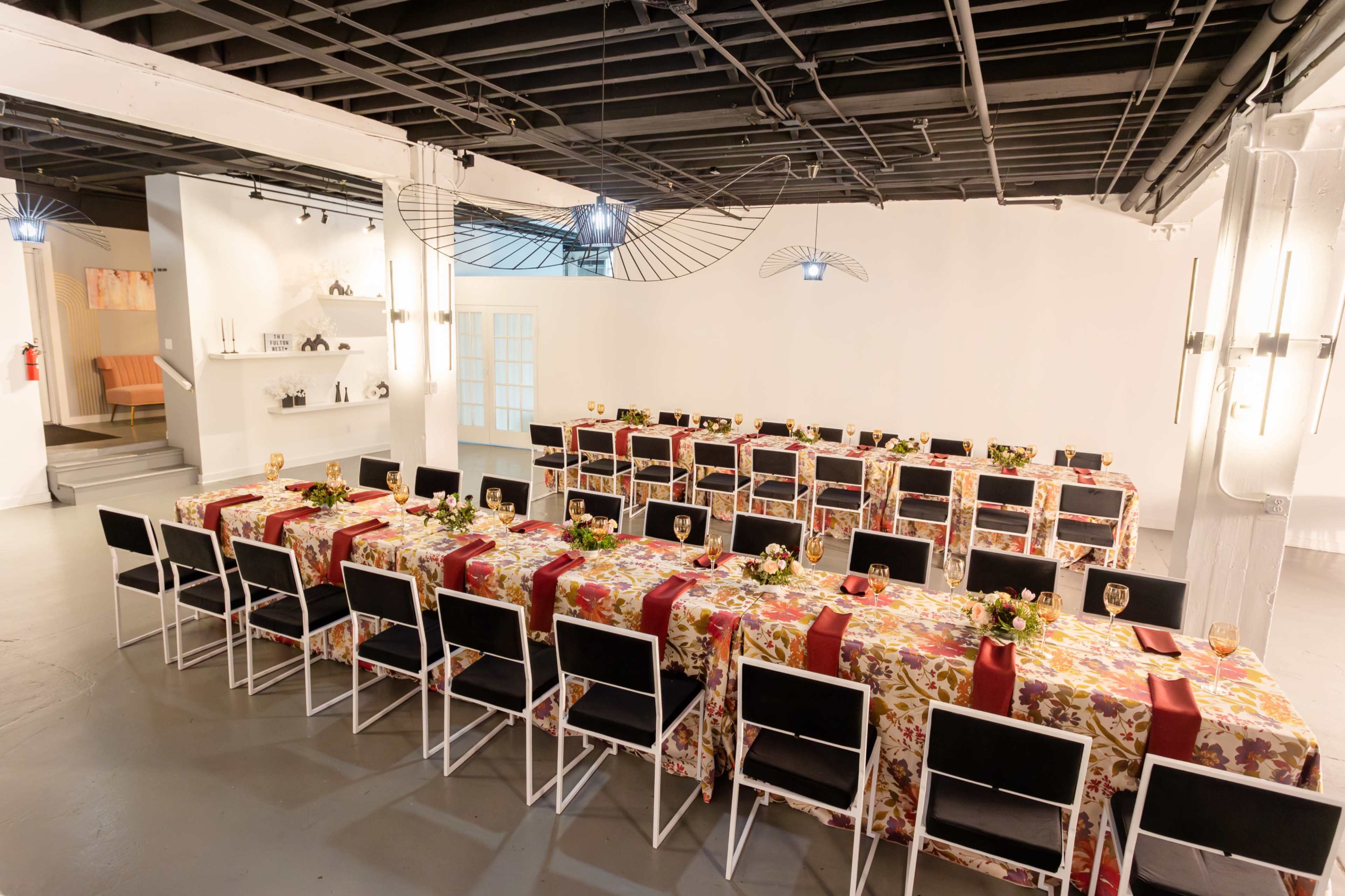 A spacious dining room features multiple long tables covered with floral tablecloths and set with place settings and glassware.