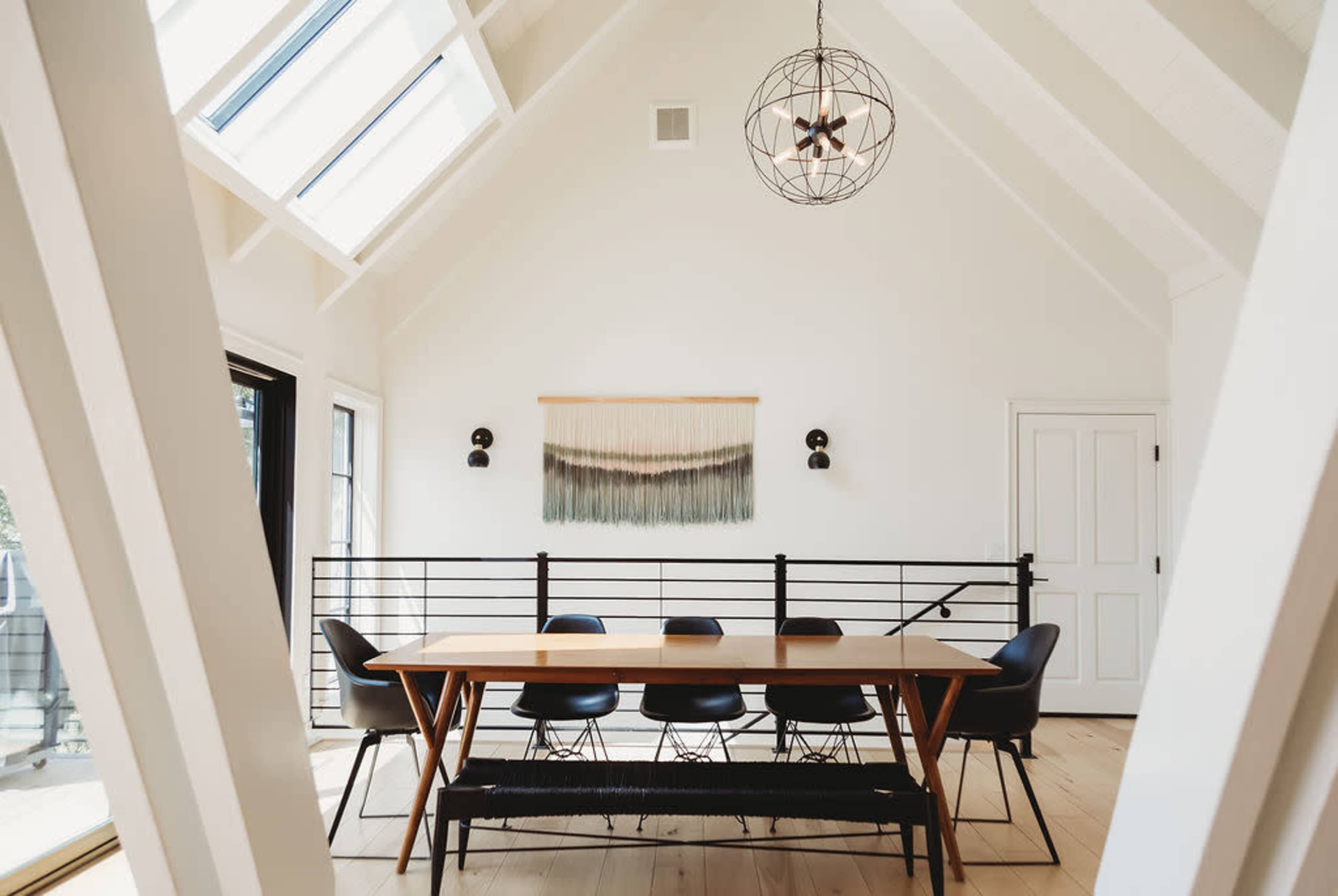 A modern dining area features a long wooden table surrounded by black chairs under a geometric pendant light.