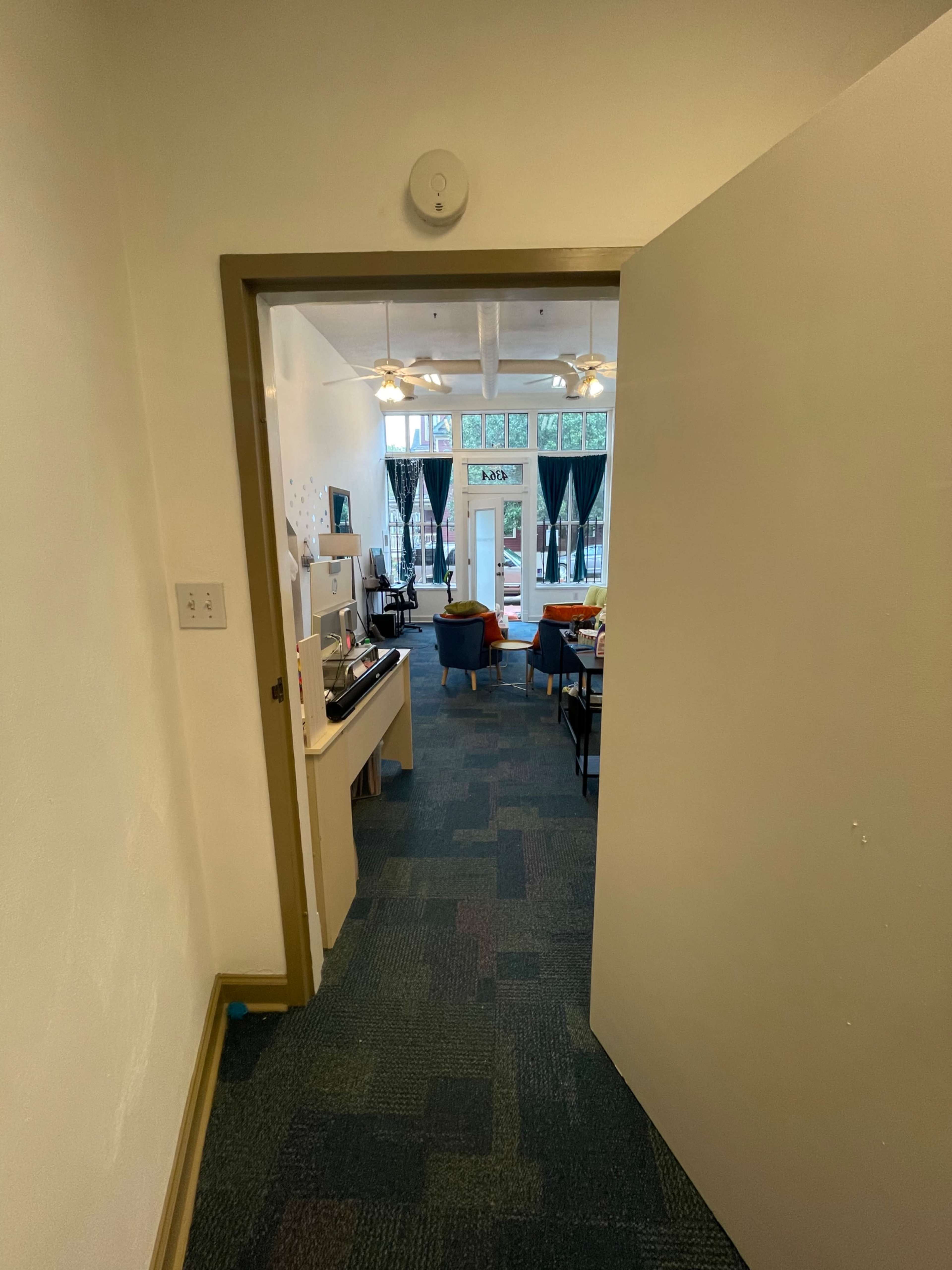 A view from a doorway into a room with a kitchenette and seating area visible through a large opening.