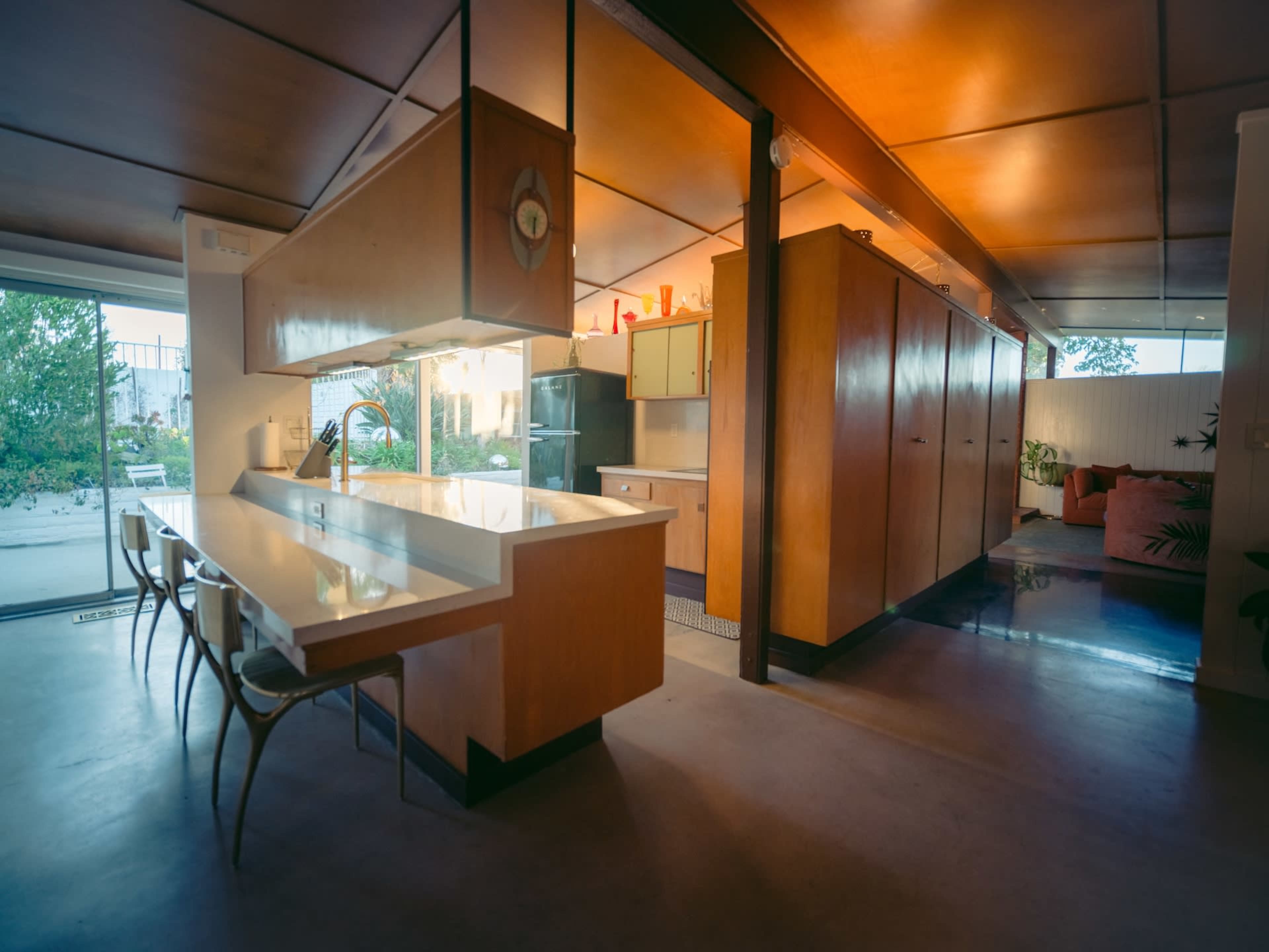 The image shows a modern kitchen with a wooden island, sleek countertops, and cabinets, designed in an open-concept layout.