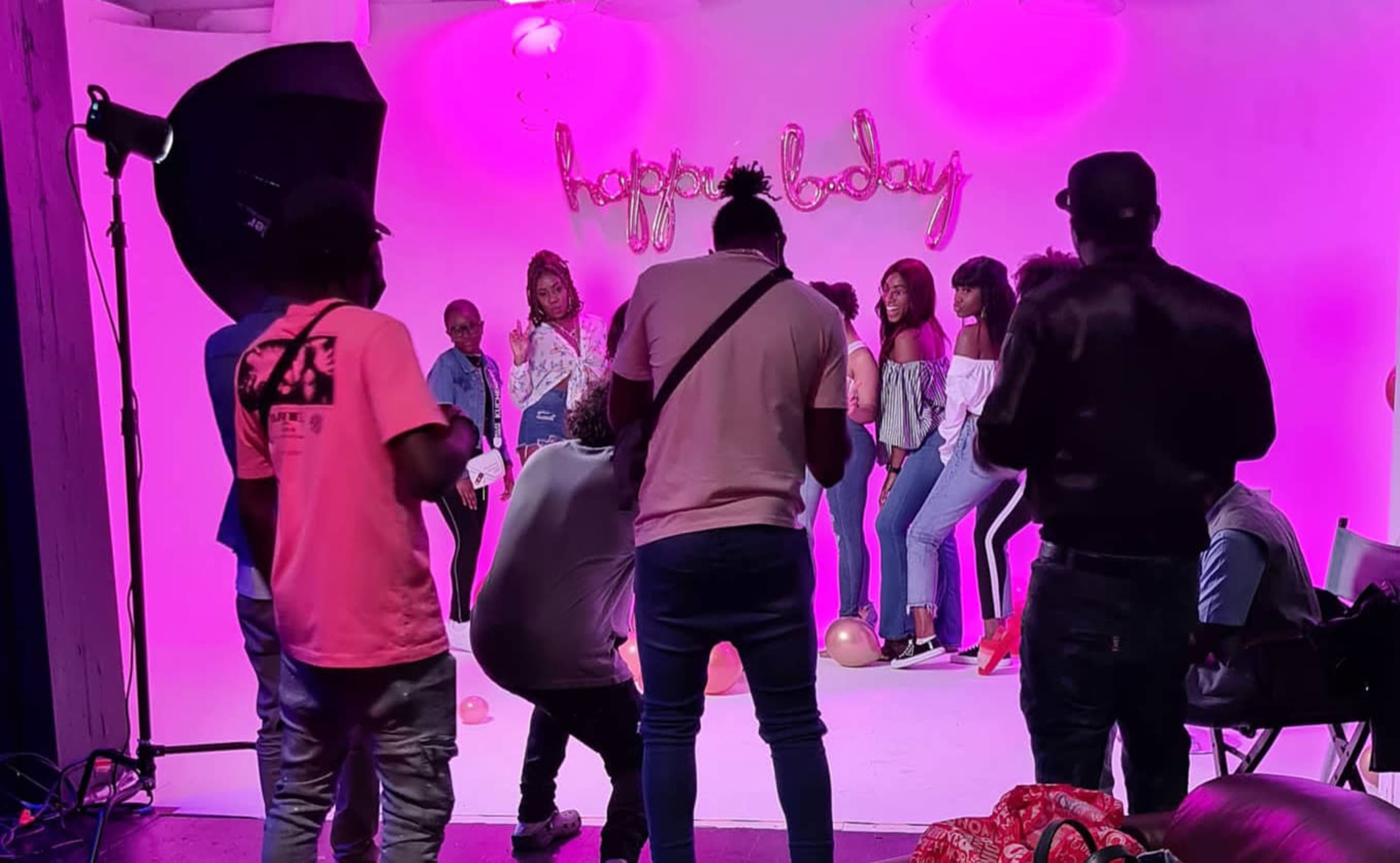 A group of people poses for a photo in front of a backdrop with "happy today" written in pink letters while a photographer captures the scene.