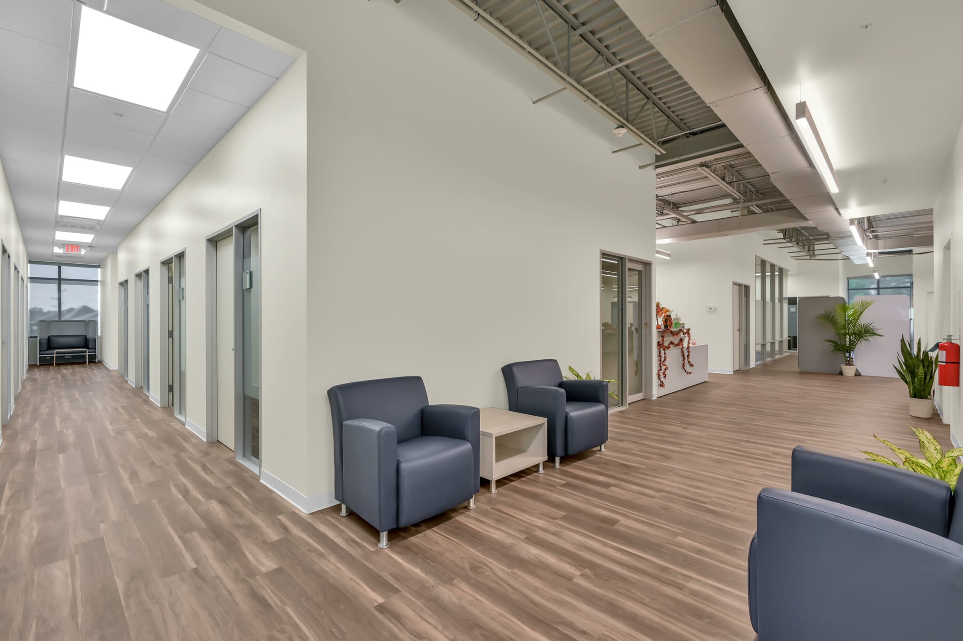 A modern office corridor with two seating areas and multiple closed office doors on either side.