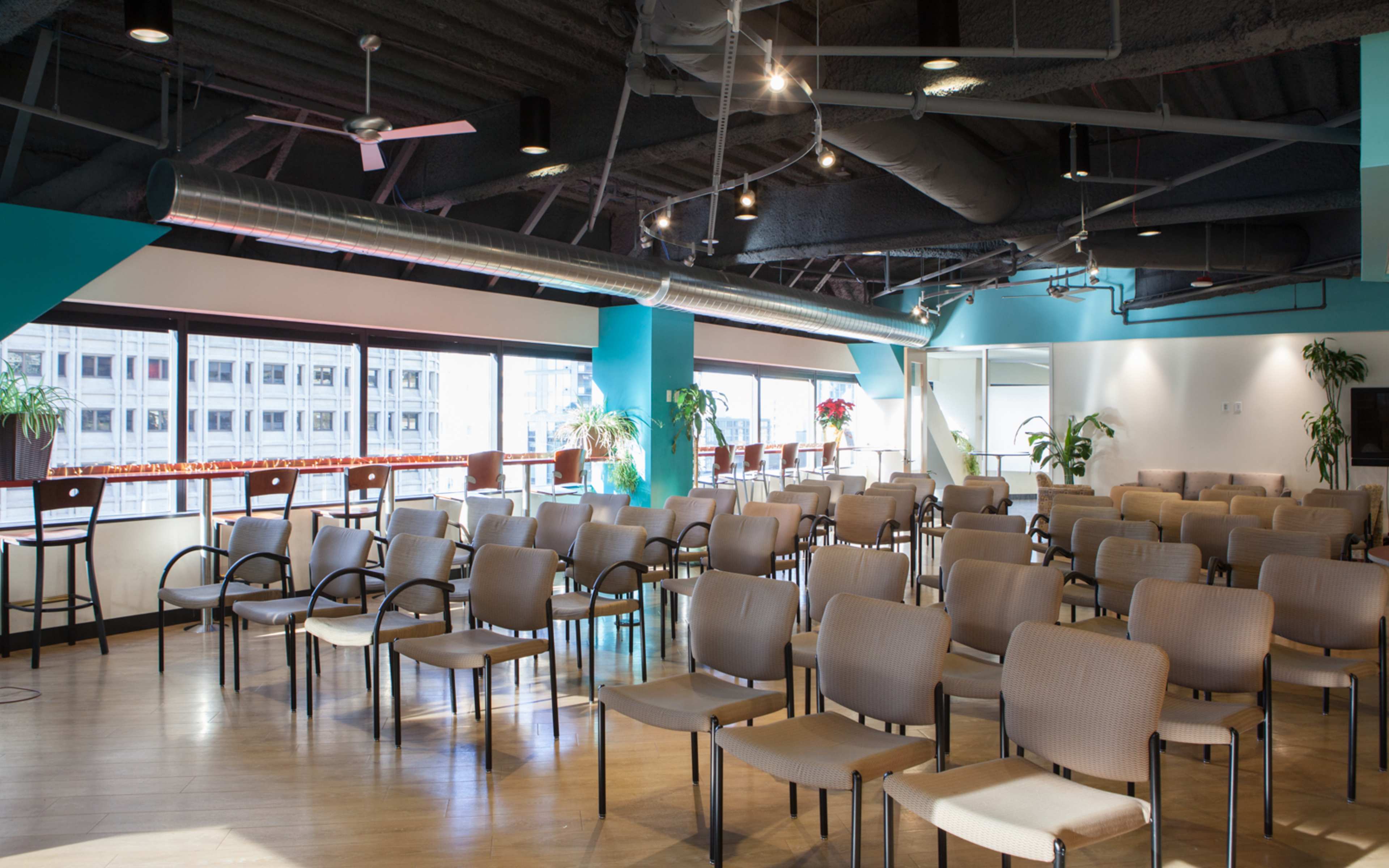 A seminar room with rows of empty chairs arranged facing a large window and a light-blue accent wall.
