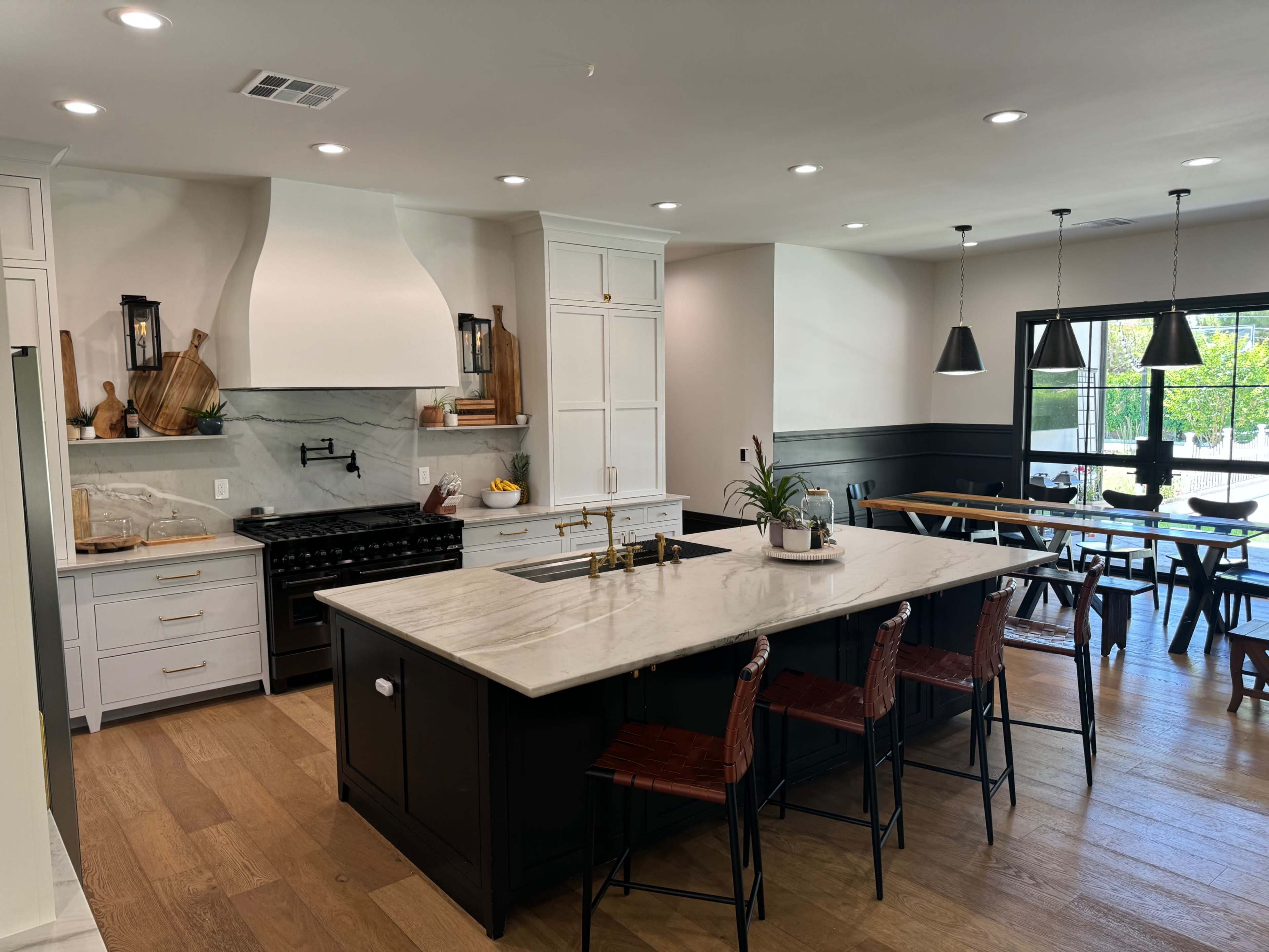 A modern kitchen with a large central island, equipped with a gas stove and white cabinetry, alongside a dining area with a wooden table and black chairs.