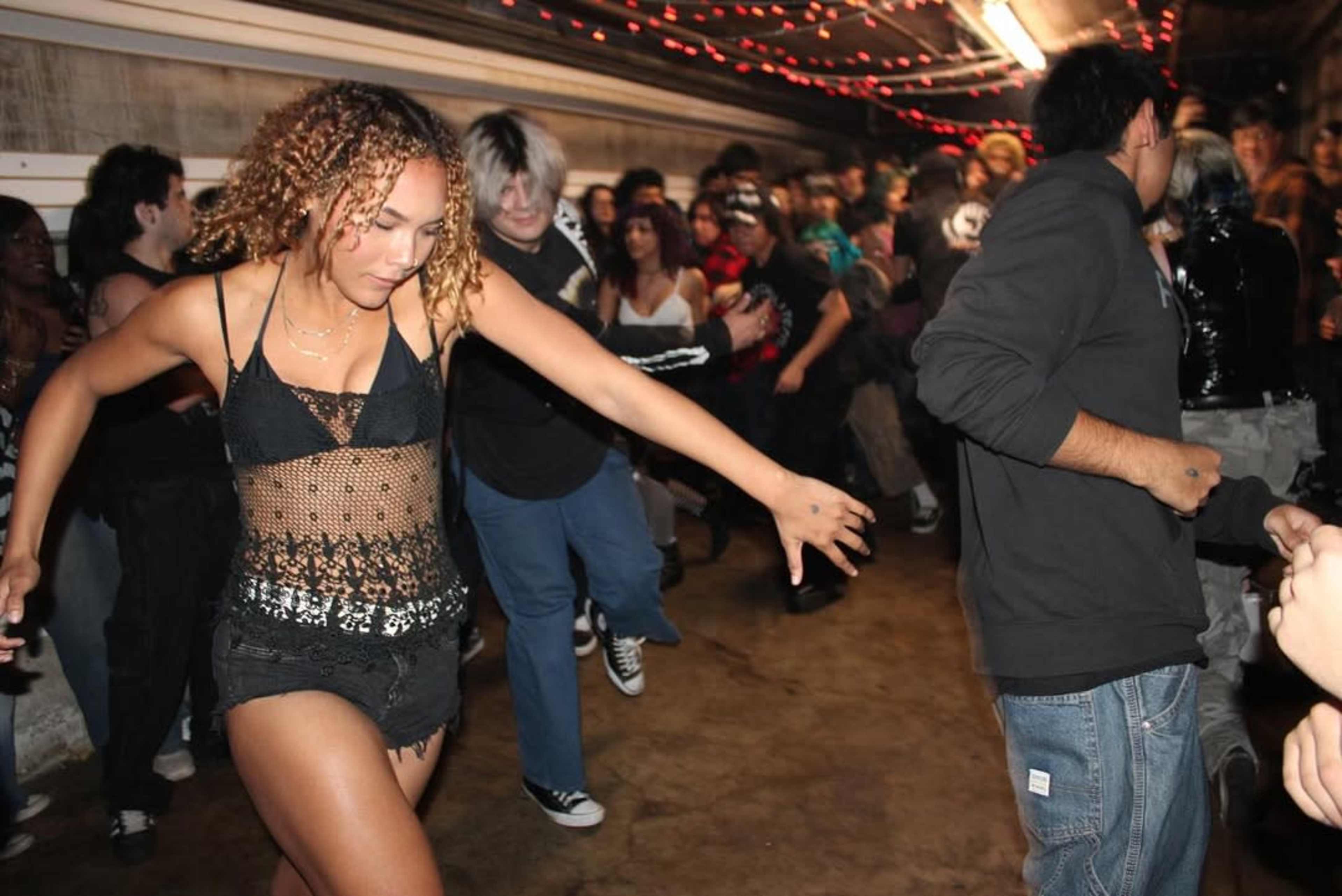 A group of people dances in a dimly lit venue adorned with string lights.
