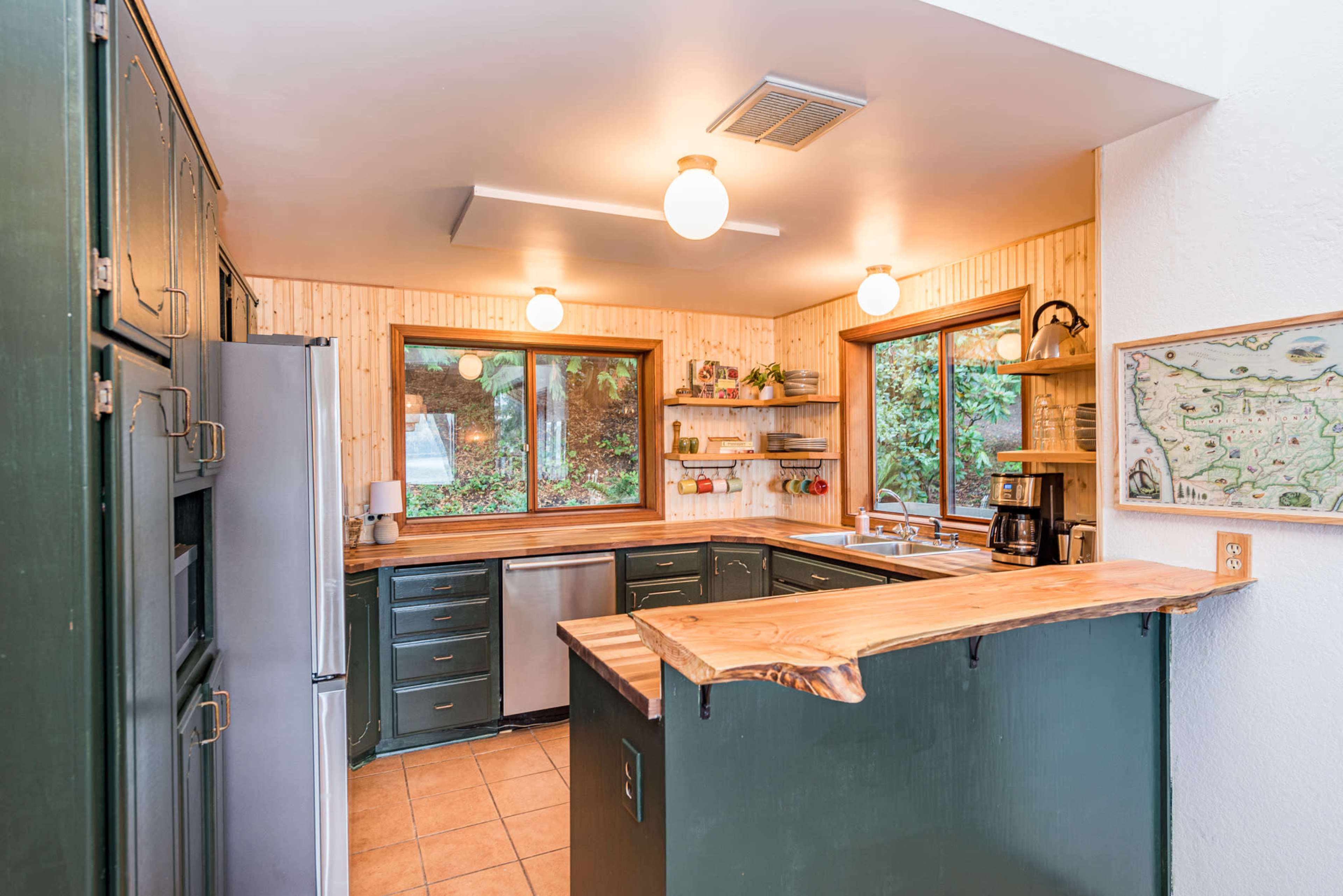 The kitchen features green cabinetry, wooden countertops, and large windows offering views of the outdoors.