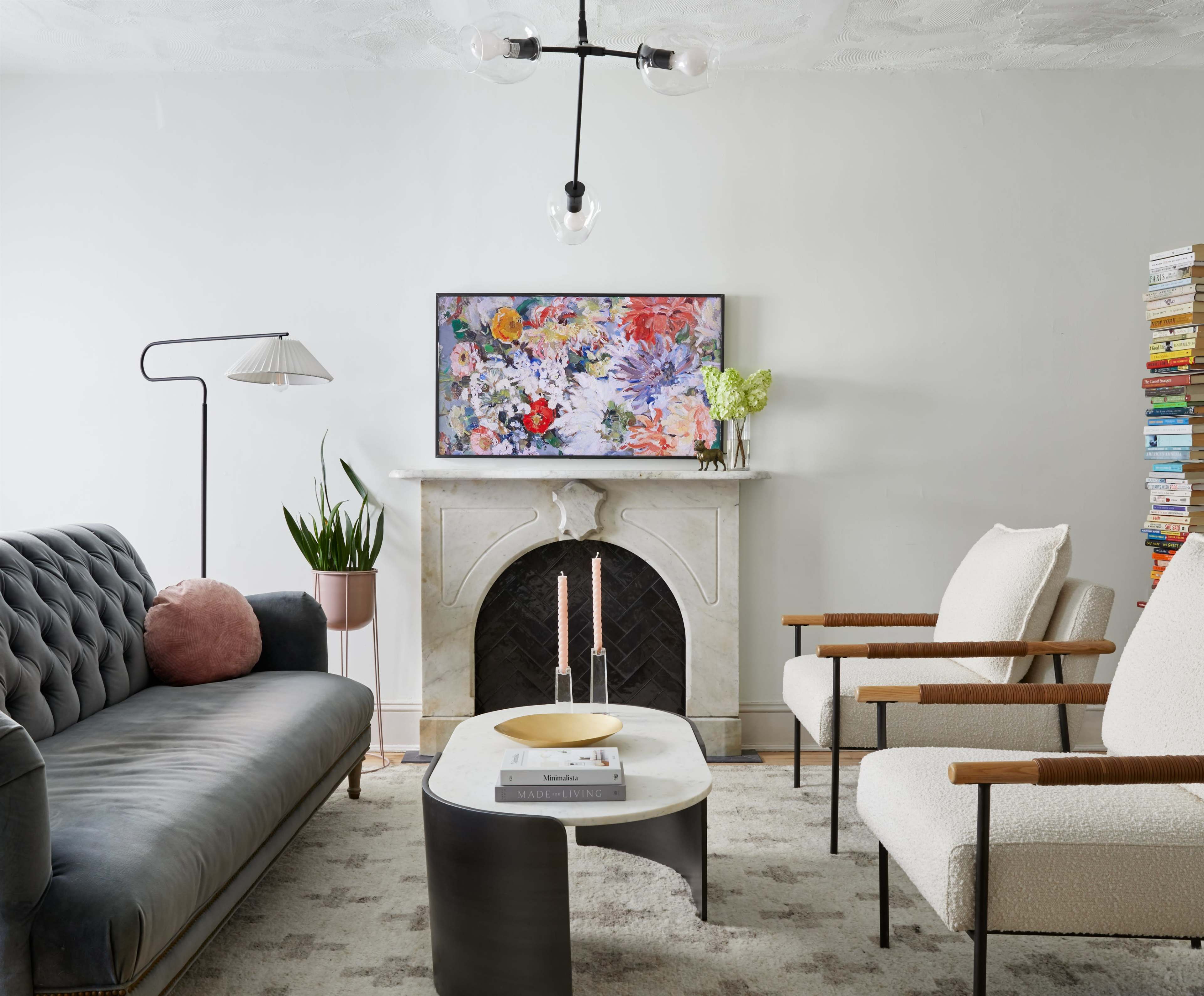 A modern living room with a sofa, two armchairs, a coffee table, and a decorative fireplace, featuring a floral artwork above it.