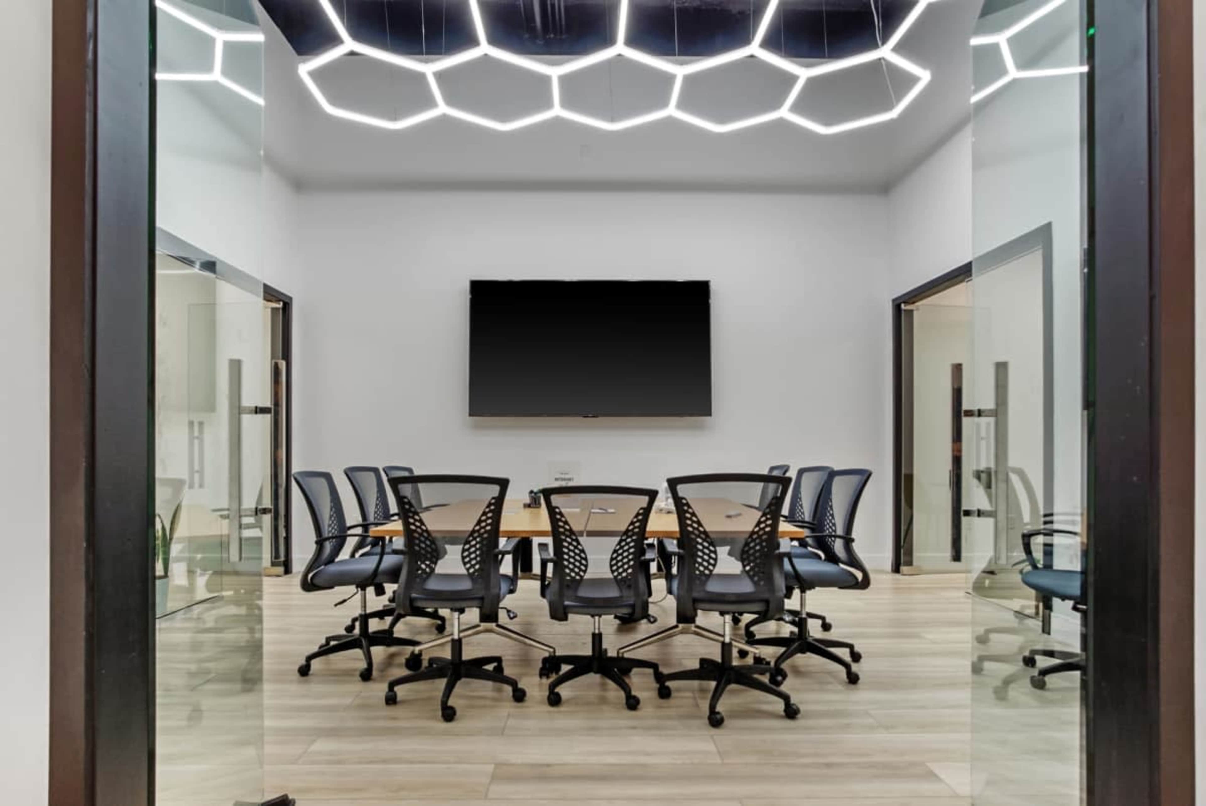 A modern conference room features a large table surrounded by rolling chairs and a wall-mounted television.