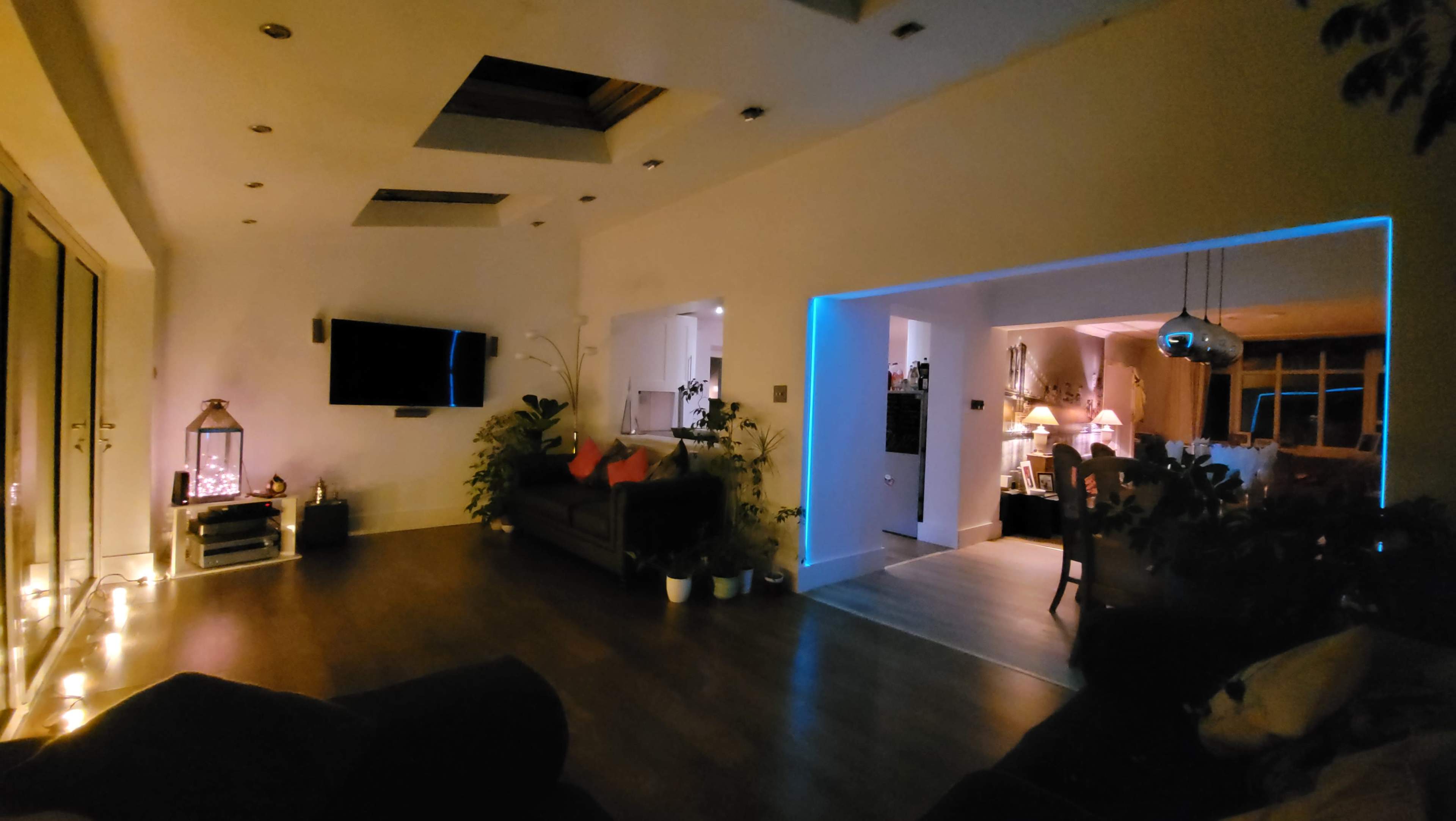A spacious living area with a television, plants, and various seating arrangements, illuminated by soft lighting.