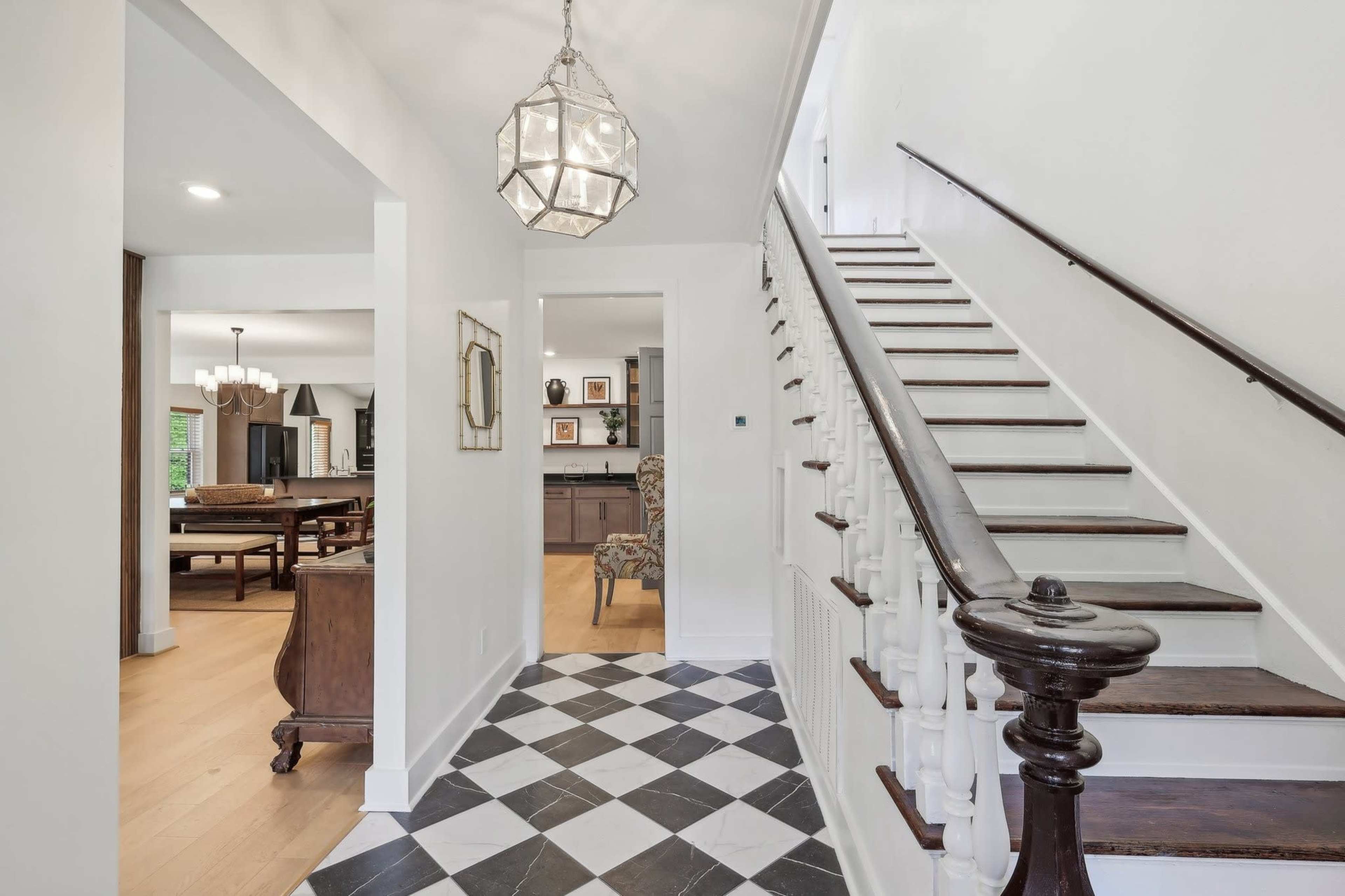 A hallway featuring a staircase with wooden railing, a patterned black-and-white floor, and a pendant light fixture.