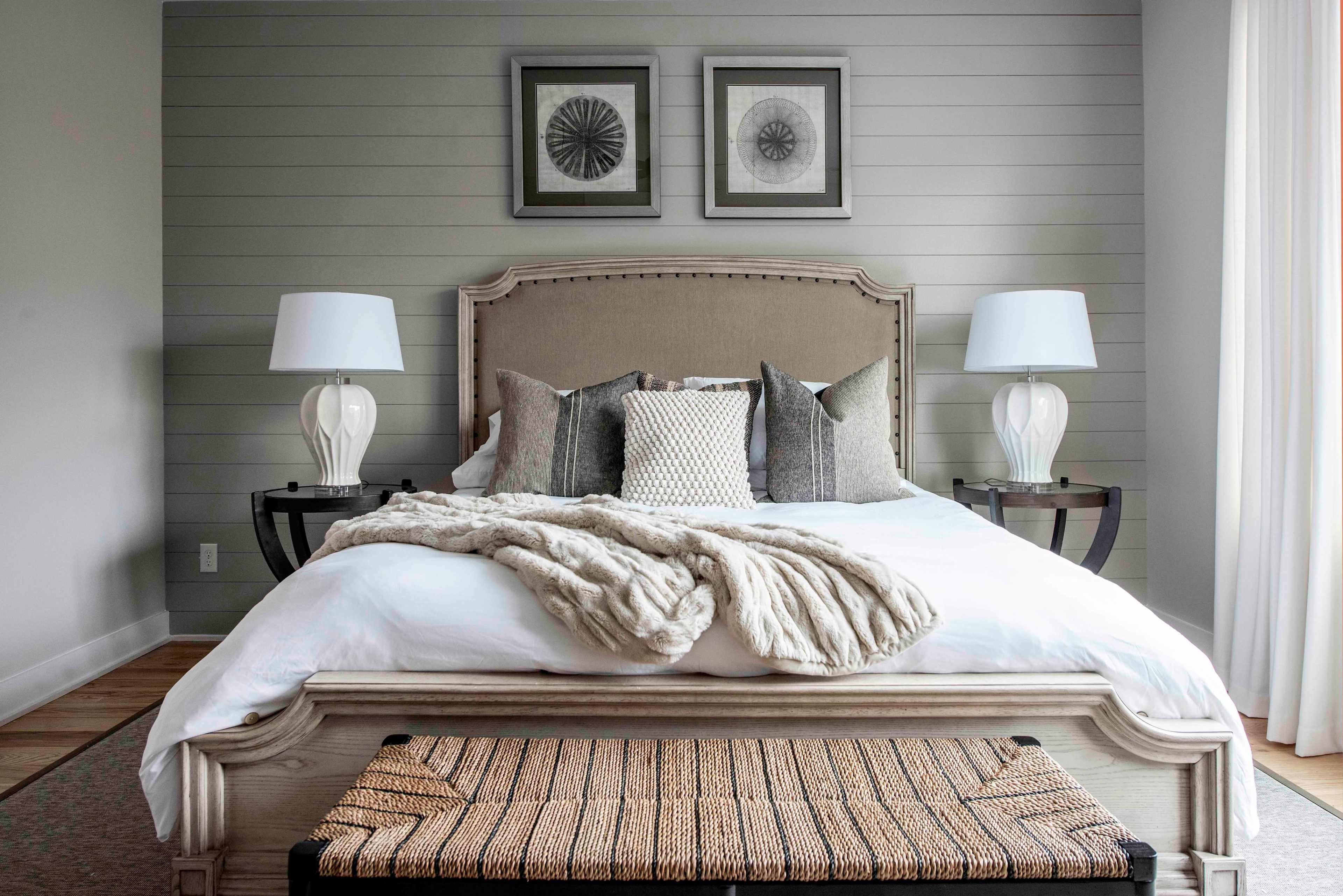 A neatly arranged bedroom features a large bed with decorative pillows, a textured throw, and matching bedside lamps on each side.