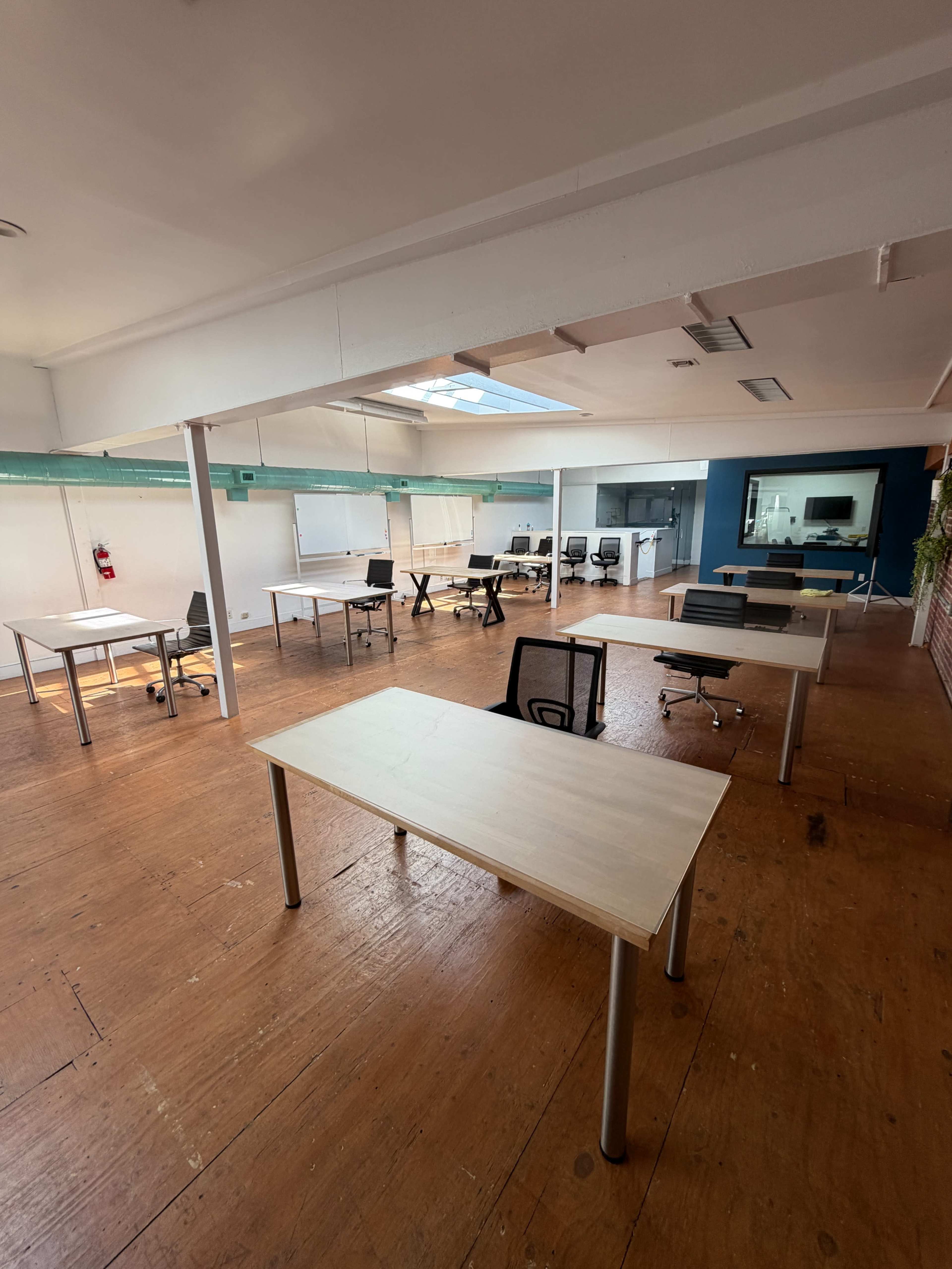 The image shows an open office space with several empty desks arranged throughout and natural light coming from a skylight.