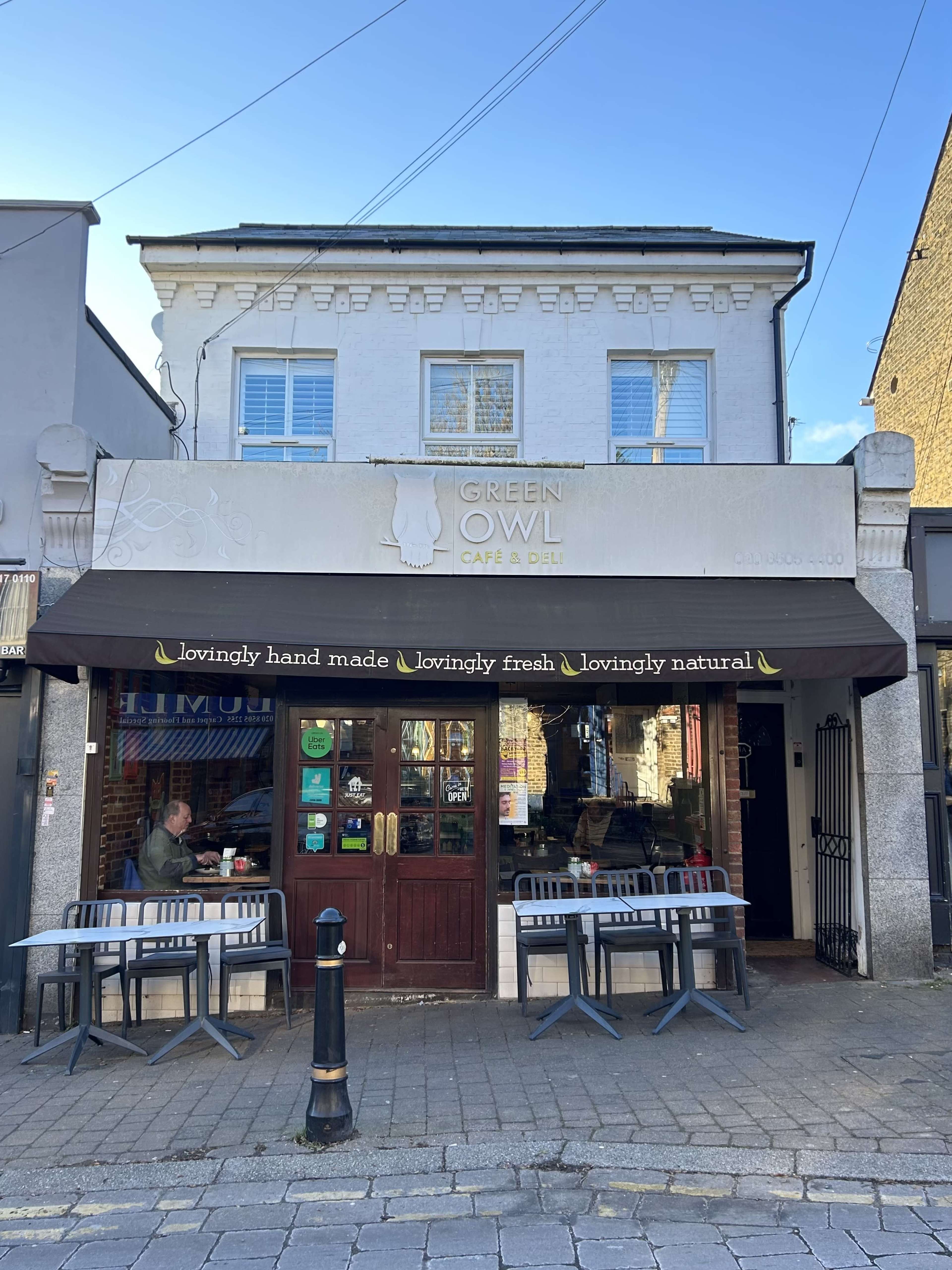 The exterior of the Green Owl Café & Deli, featuring a sign above the entrance and outdoor seating arrangements.