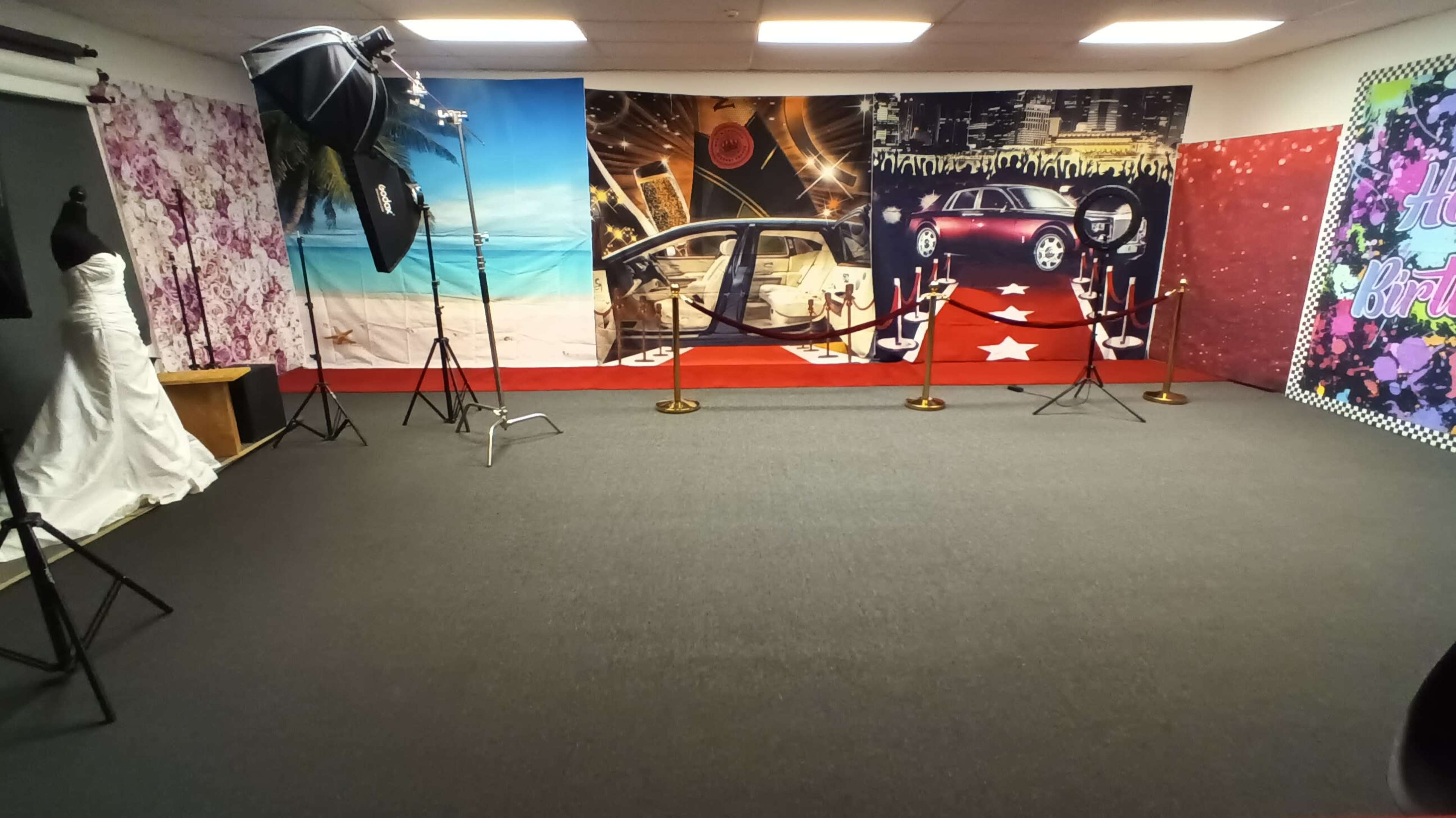 The image shows a photo studio set up with a red carpet, star decorations, backdrops featuring cityscapes and floral designs, and lighting equipment arranged around the space.