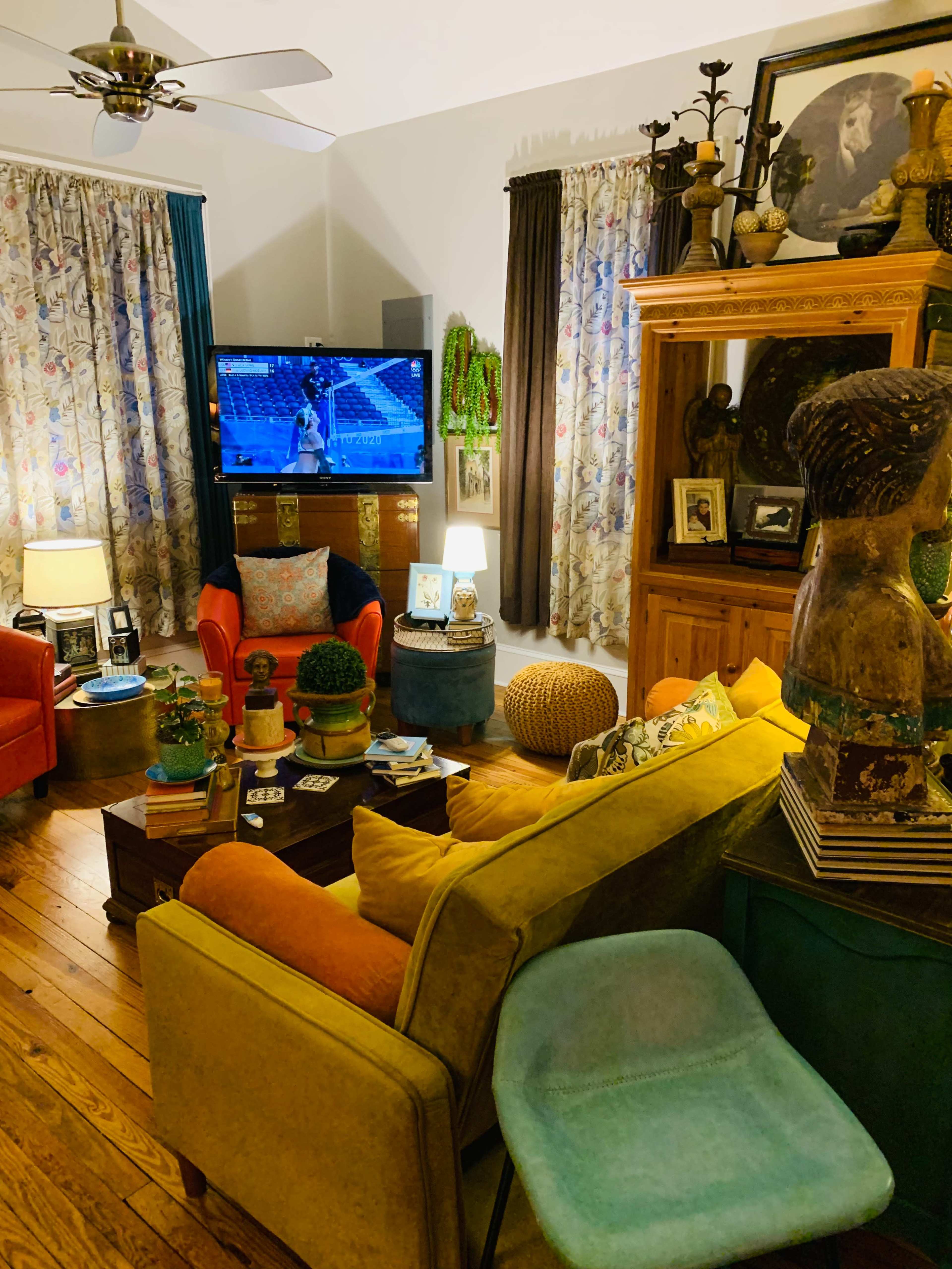A cozy living room features colorful furniture, a television displaying a sports game, and various decorative elements on shelves and tables.