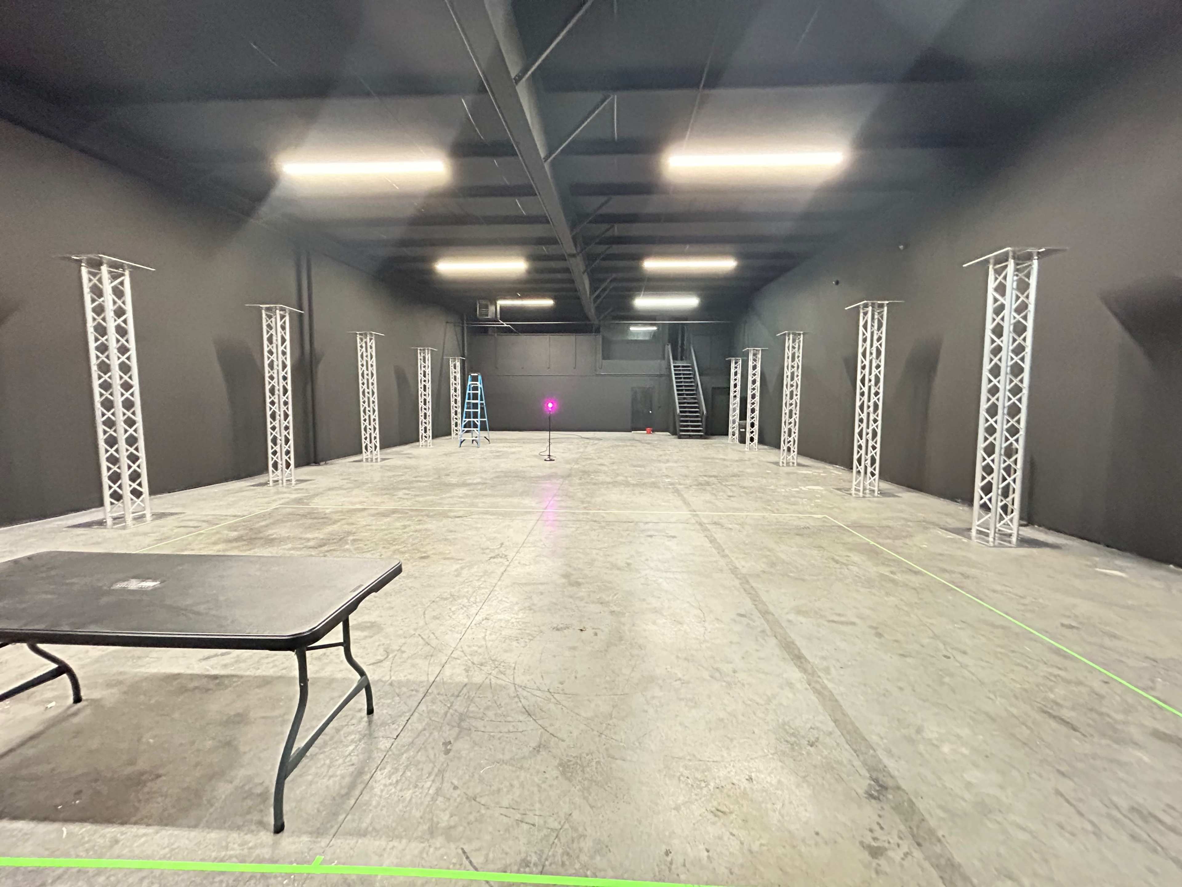 An empty industrial space with a concrete floor, black walls, and several tall, white truss structures arranged around the room.