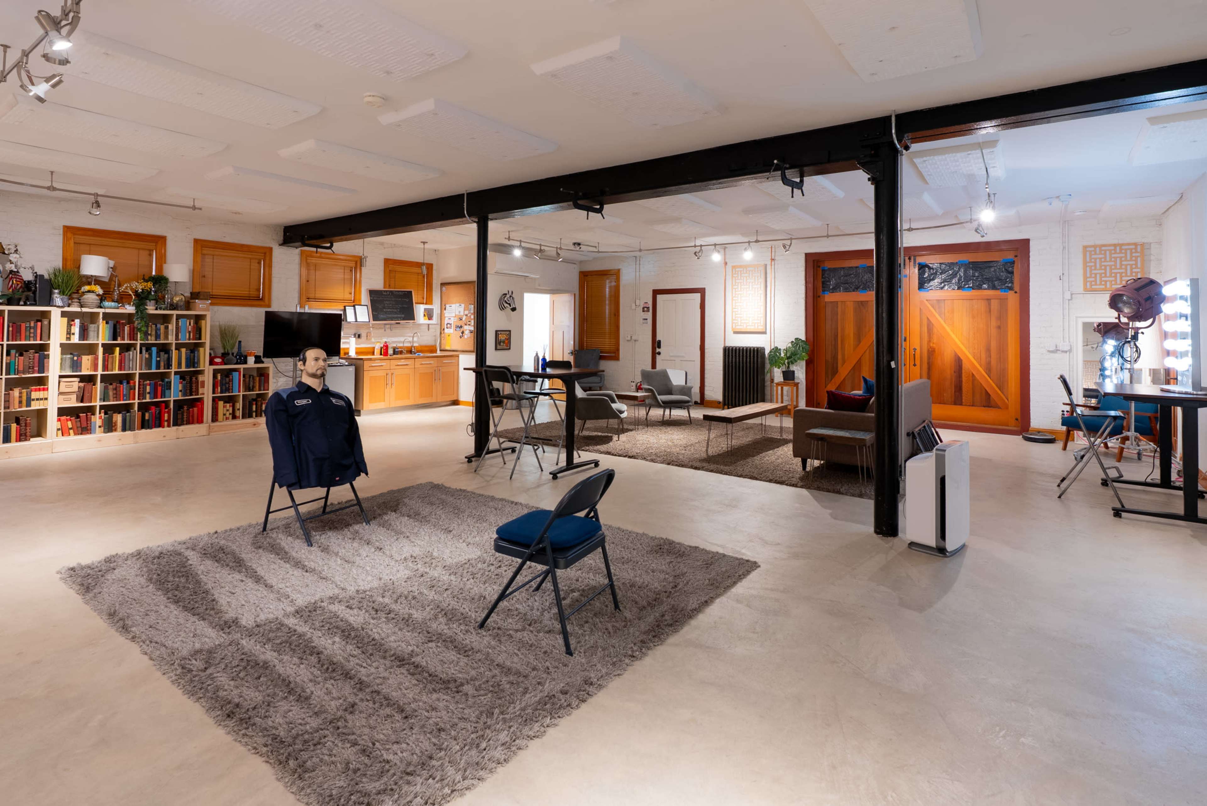 The image shows a spacious, modern interior featuring a living area with a large rug, a dining table, and a well-equipped kitchen in the background.