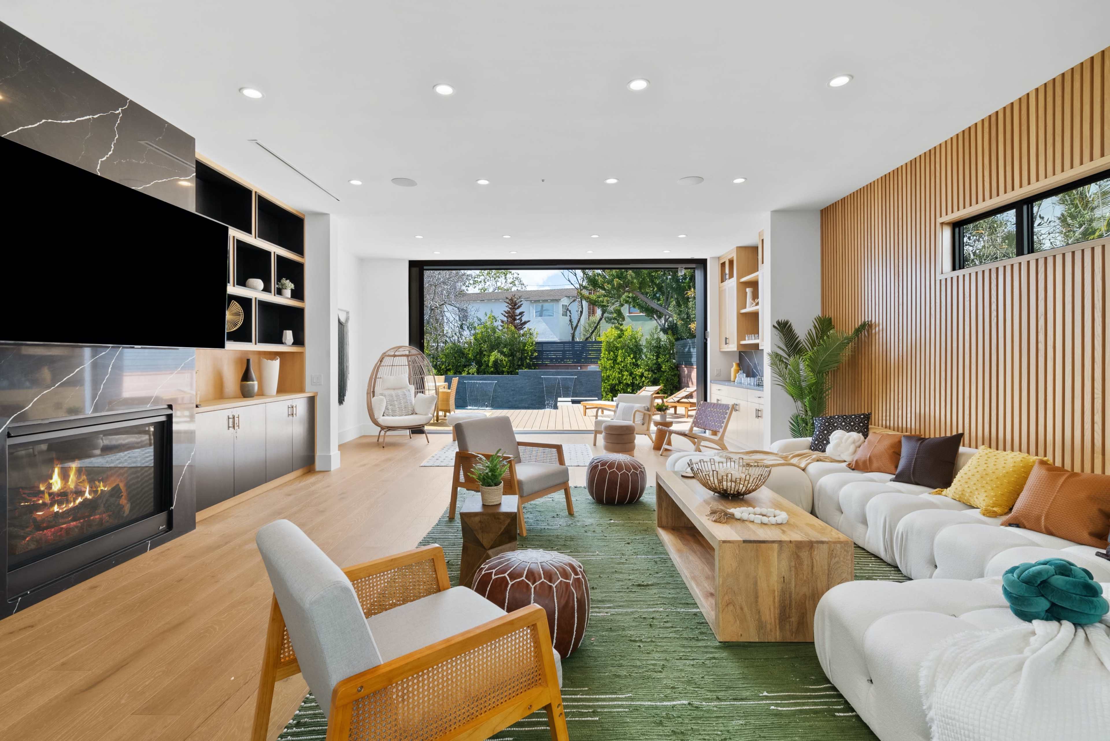A modern living room features sleek furniture, a large window overlooking an outdoor area, and a central fireplace.