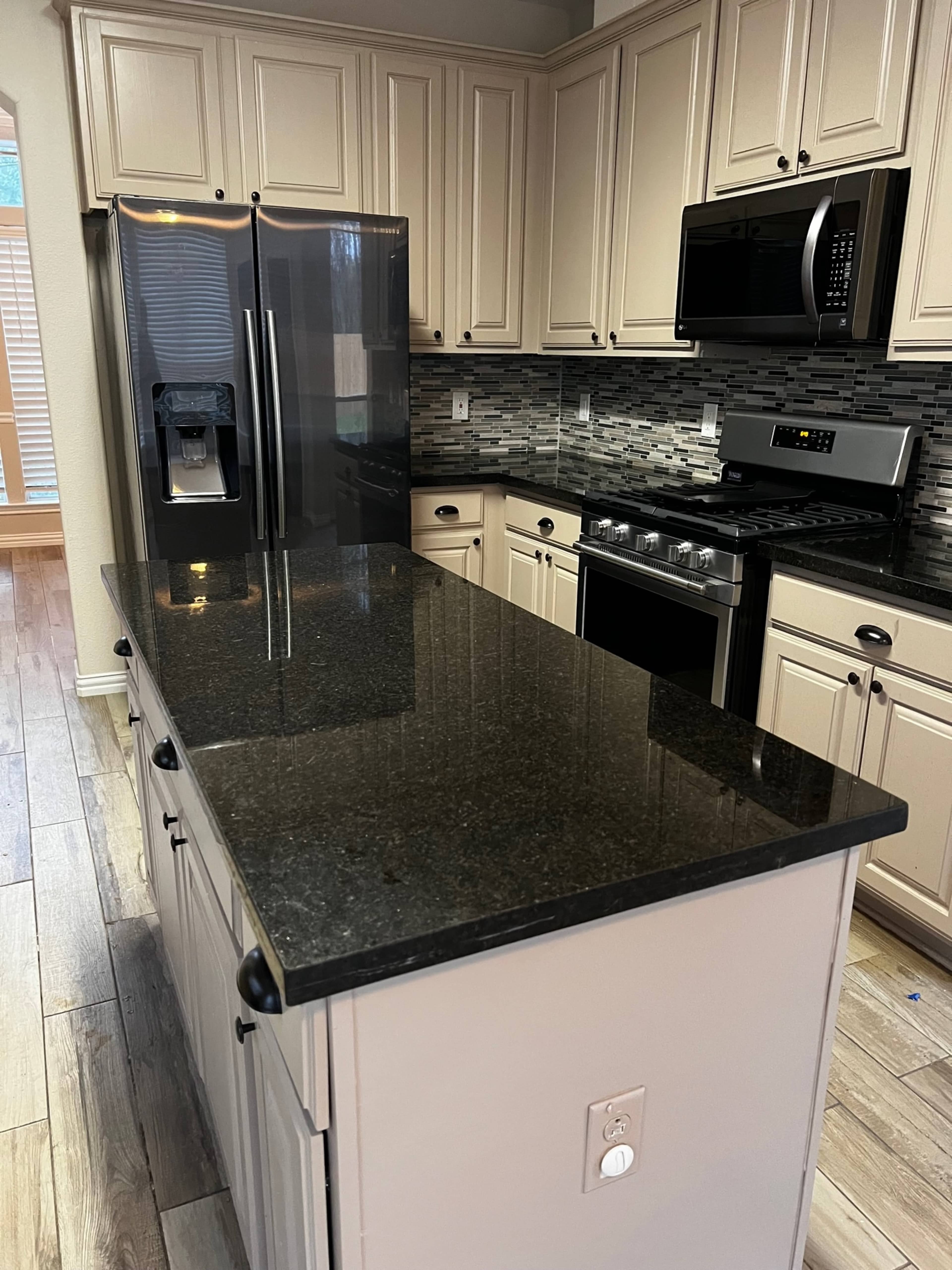 A modern kitchen with dark countertops, stainless steel appliances, and light-colored cabinetry.