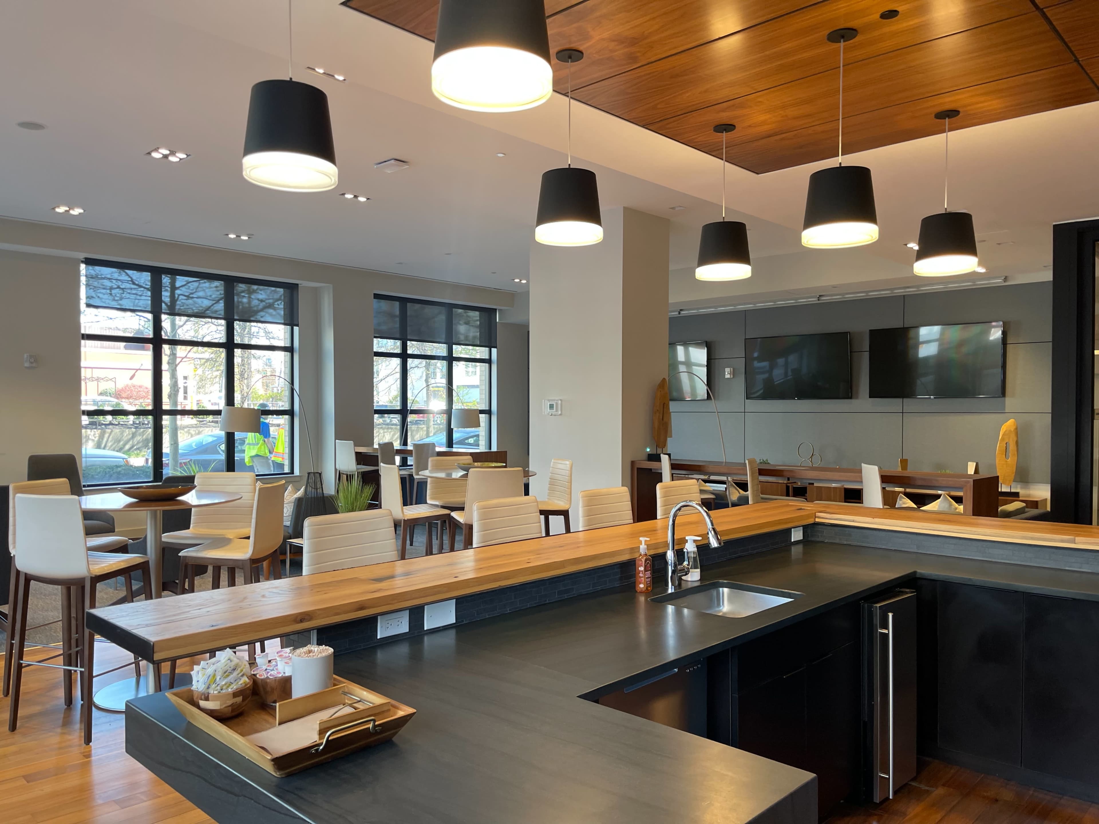 A modern café interior featuring a wooden counter, high-top tables, and pendant lighting.