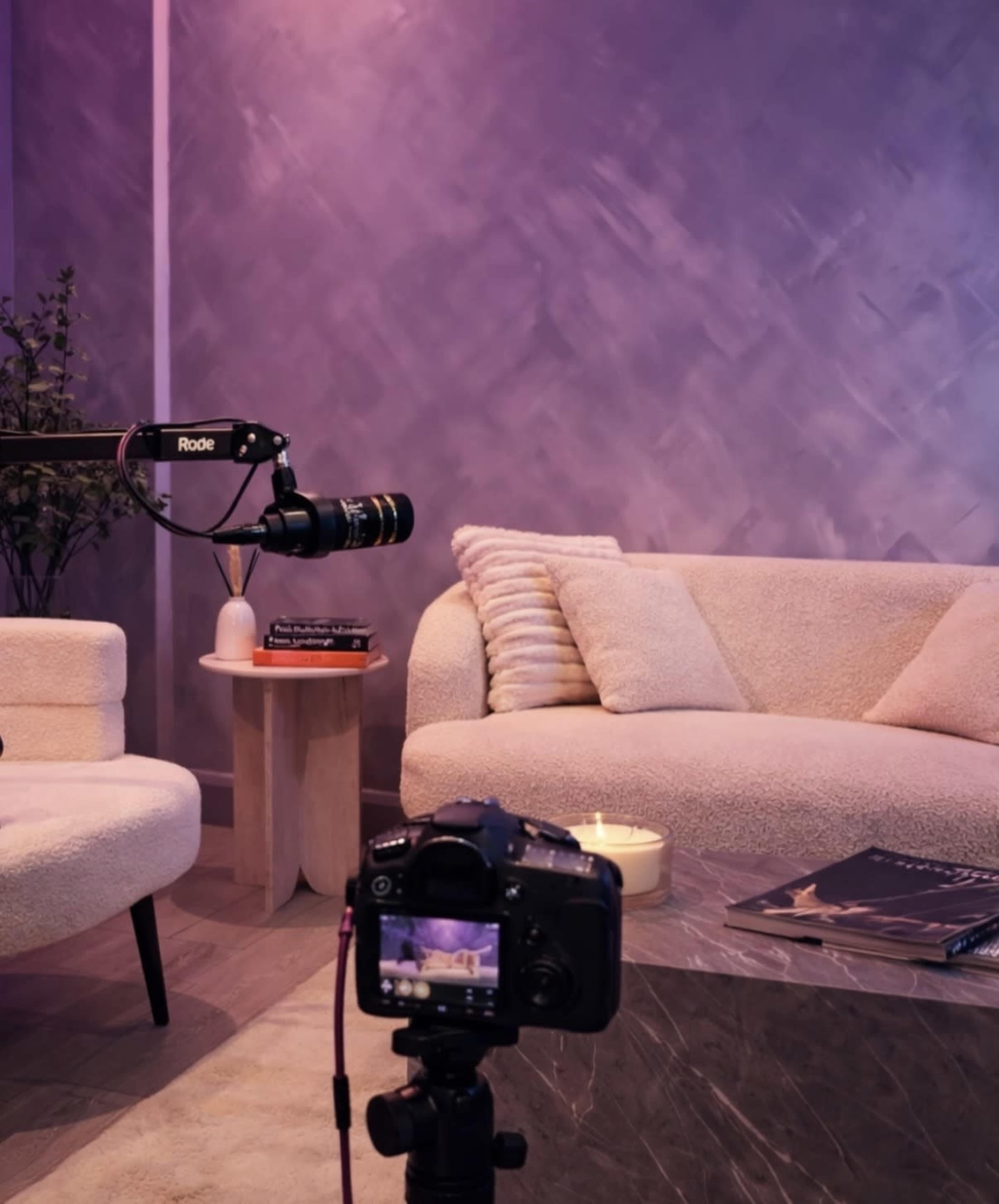 A camera is positioned on a tripod facing a cozy, softly lit living room with a modern couch, a small table, and decorative items.