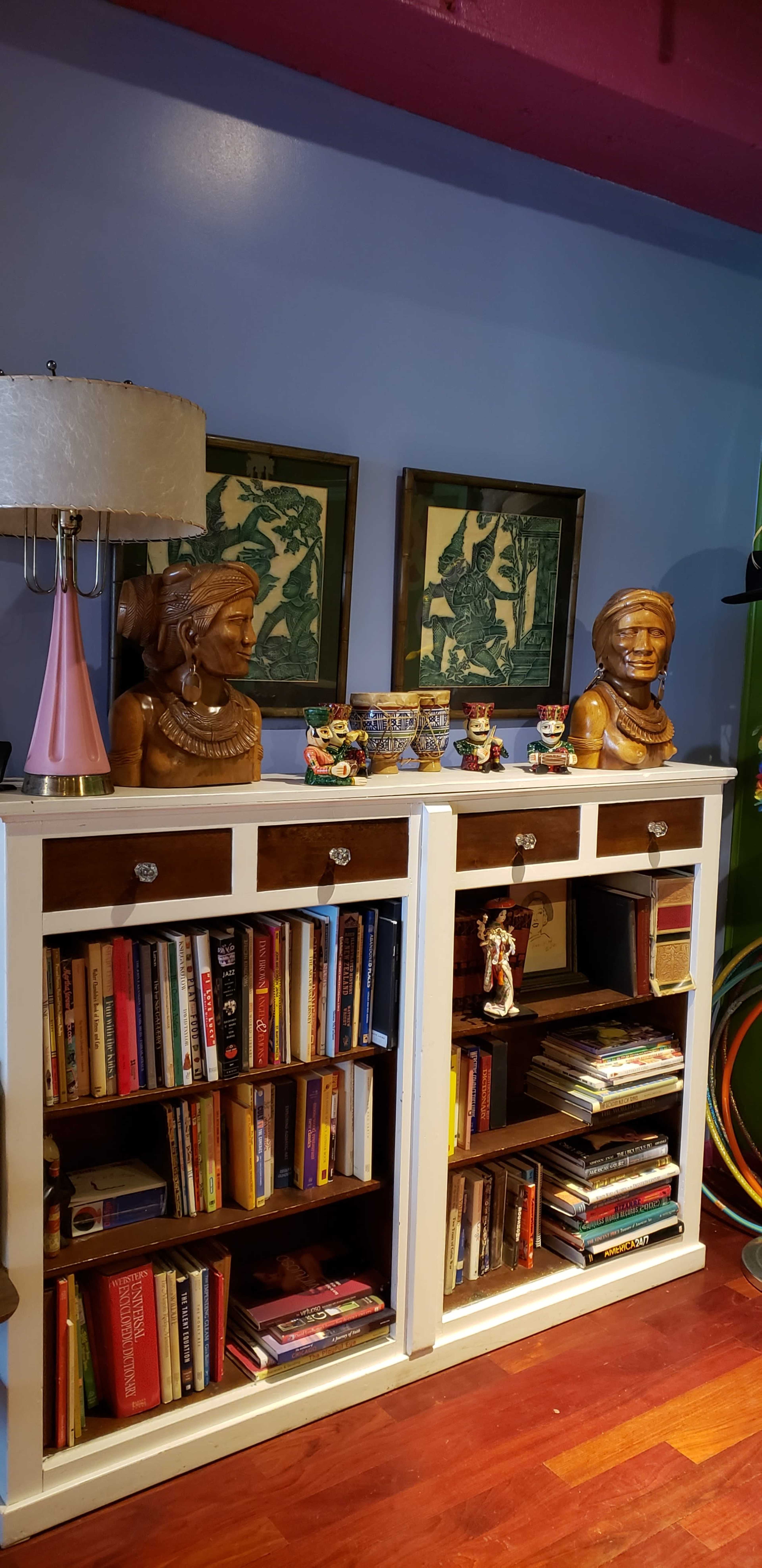 A bookshelf adorned with decorative sculptures, framed artwork, and various books, set against a blue wall.