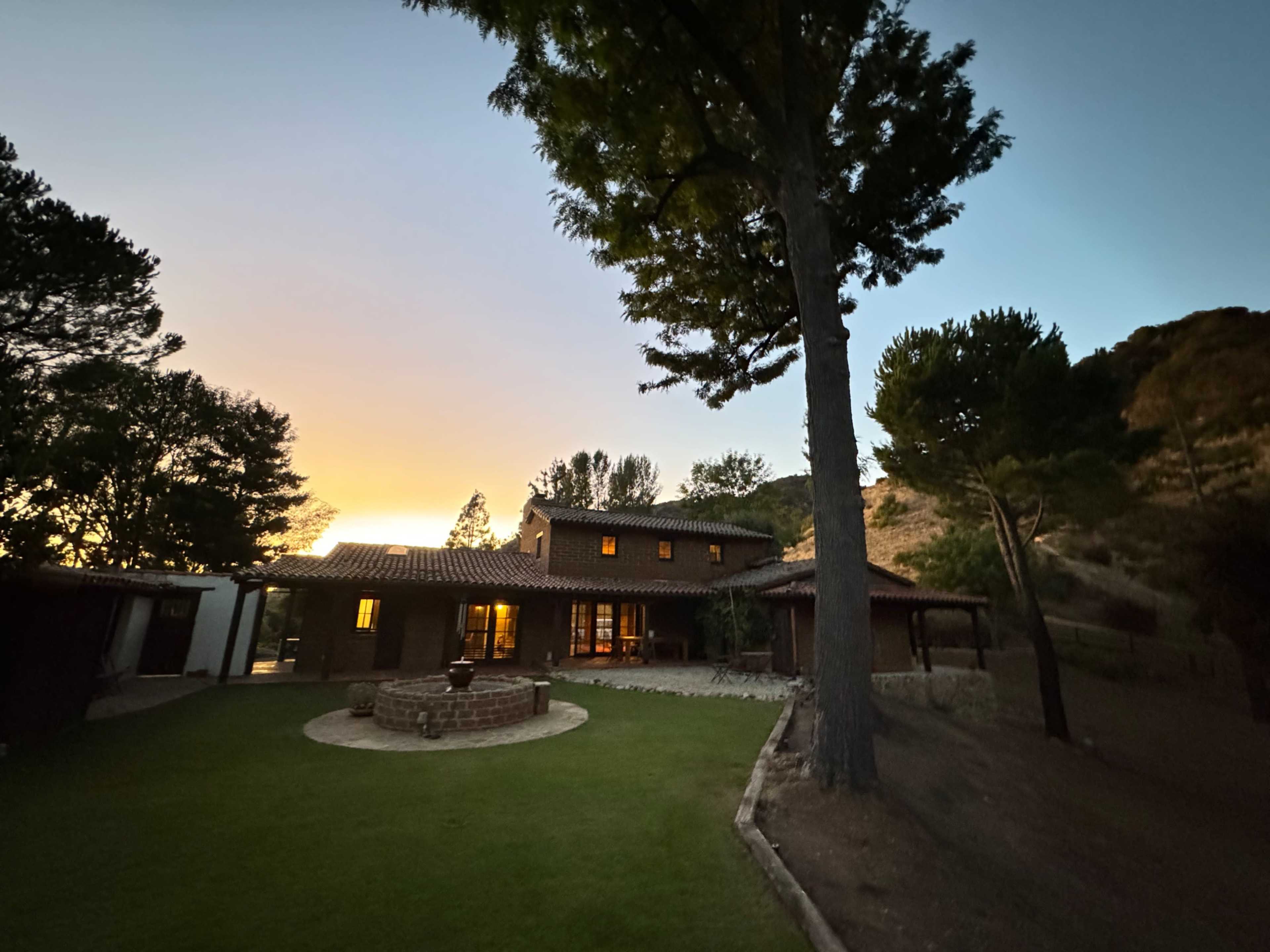 The image shows a two-story house with a brick exterior, surrounded by trees, and illuminated by sunset in the background.