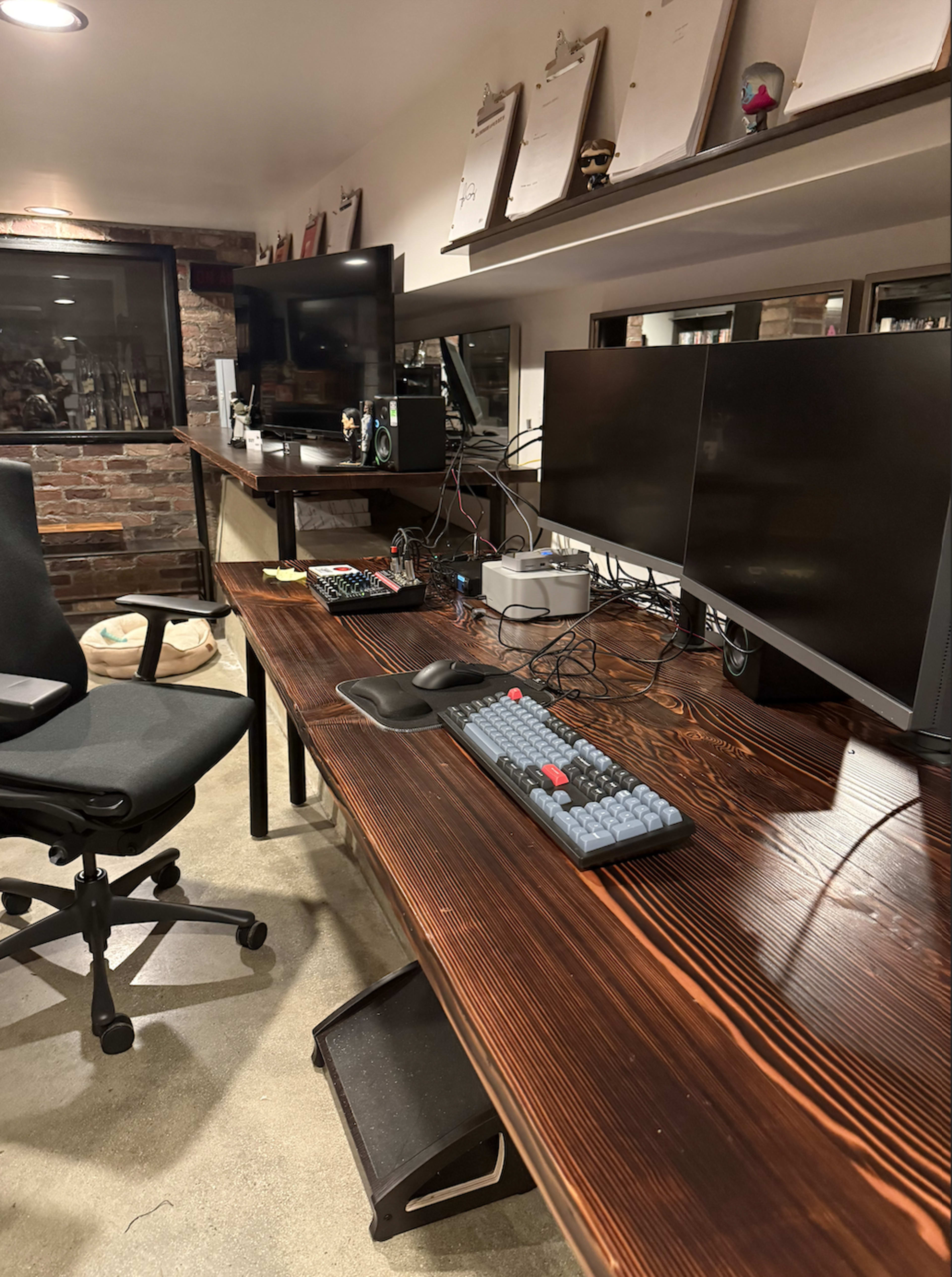 The image showcases a modern workspace with a large wooden desk, multiple monitors, a mechanical keyboard, and a black office chair.