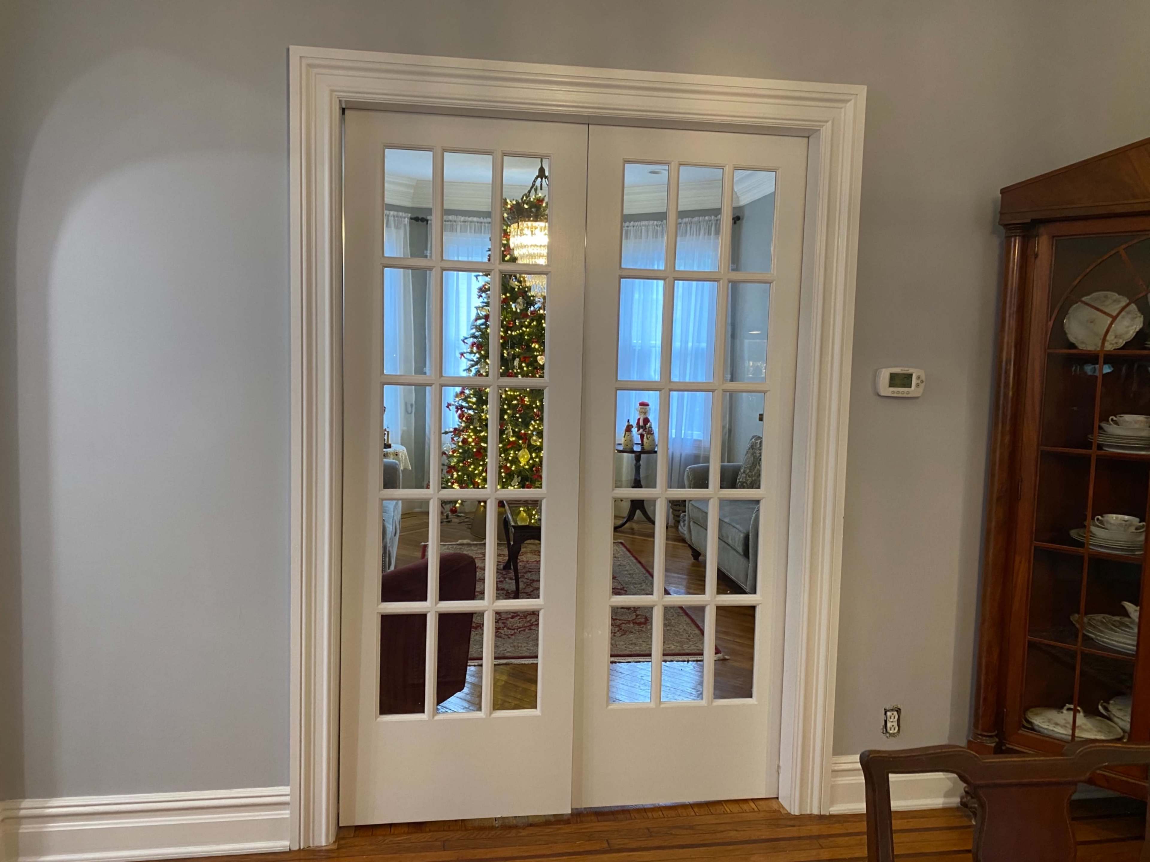 A set of double doors with glass panels leads to a room featuring a decorated Christmas tree and cozy furniture.